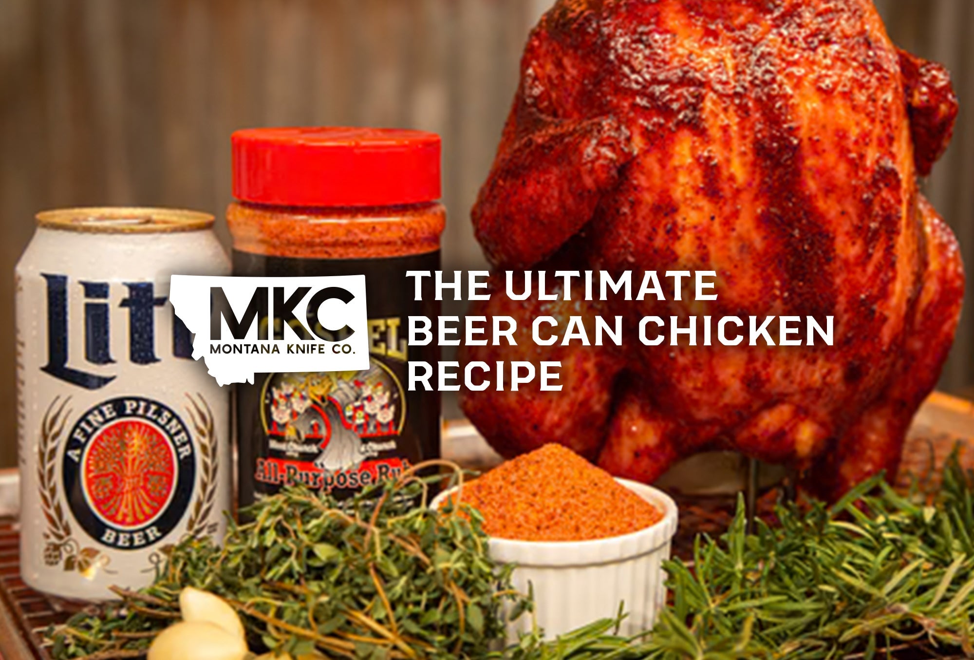 Seasoned whole chicken, positioned upright beside a bottle of seasoning, a beer can, and sprigs of fresh herbs.