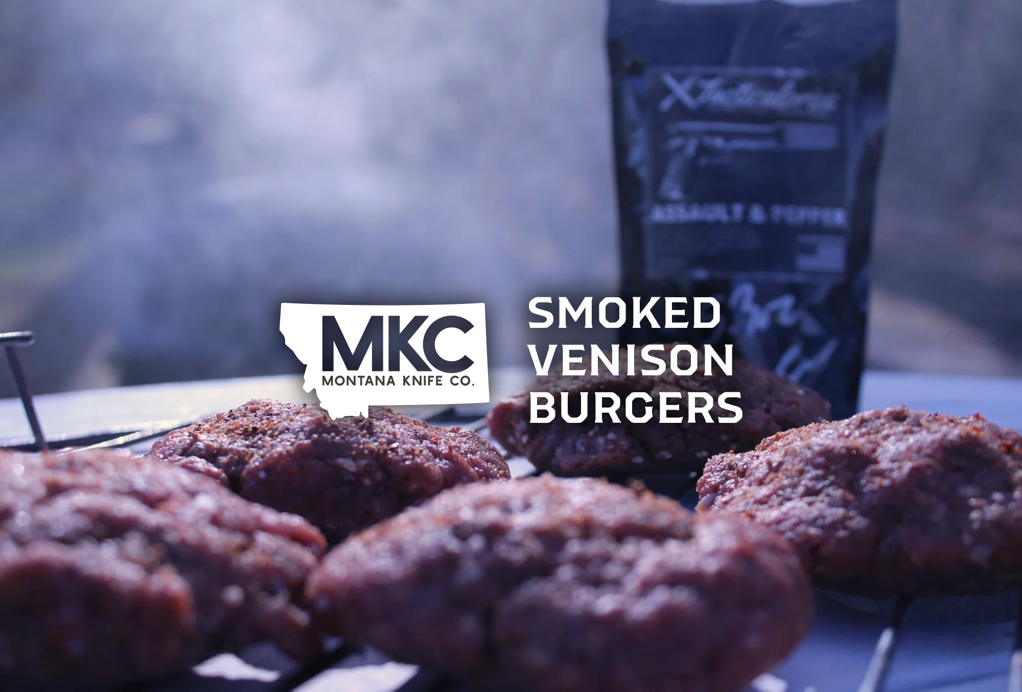 Close-up of smoked venison burgers cooking on a grill with smoke rising.