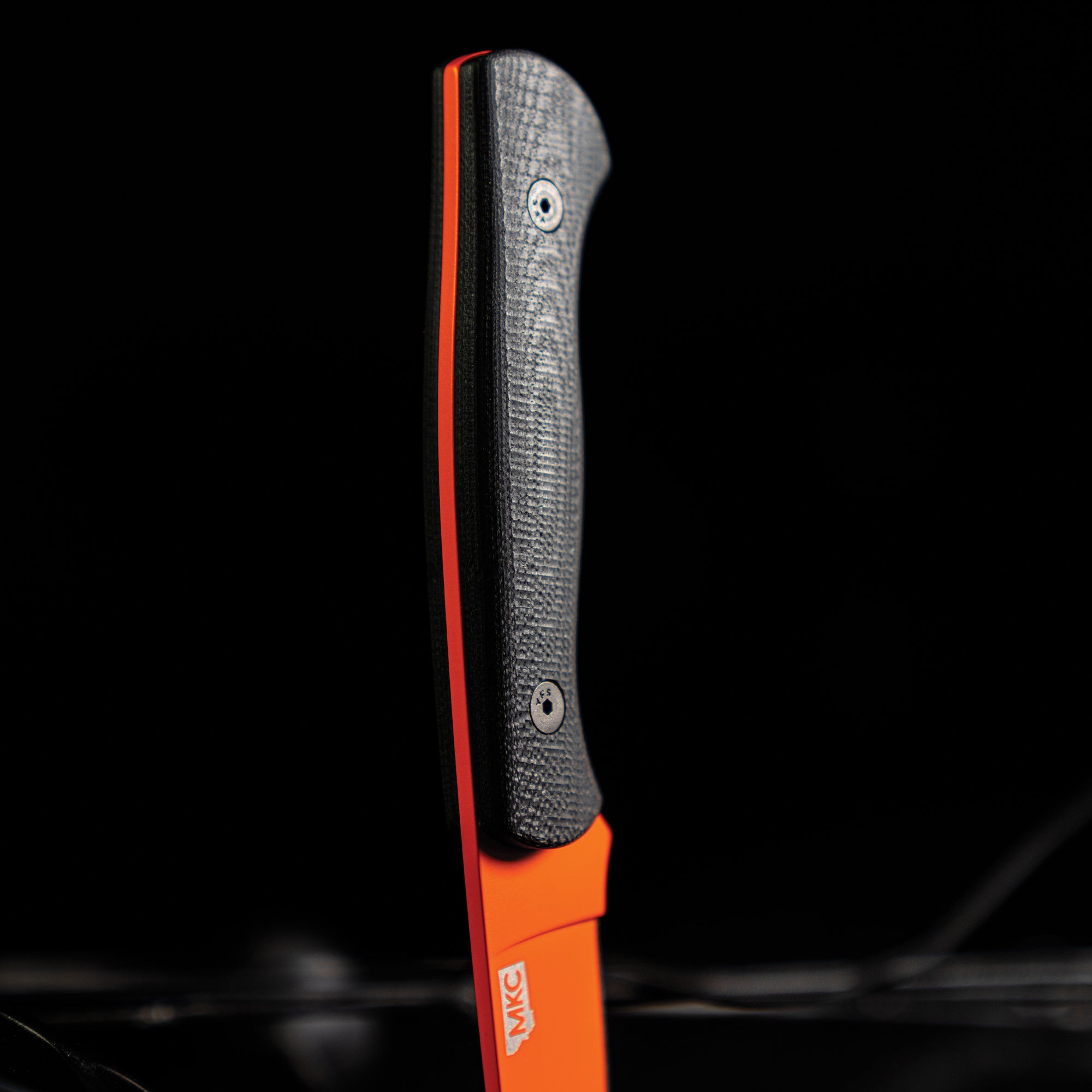 Close-up of a BLACKFOOT 2.0 knife with a blaze orange Cerakote handle and textured grey grip, showcased against a dark background.