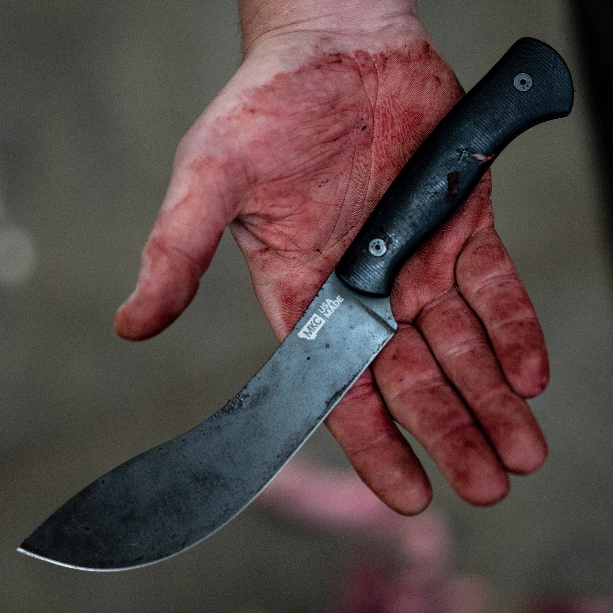 Alt text: "Close-up of a used Beartooth Pro Skinning Blade with a black handle, held in a hand covered in blood, highlighting the blade's effectiveness and sturdy grip."