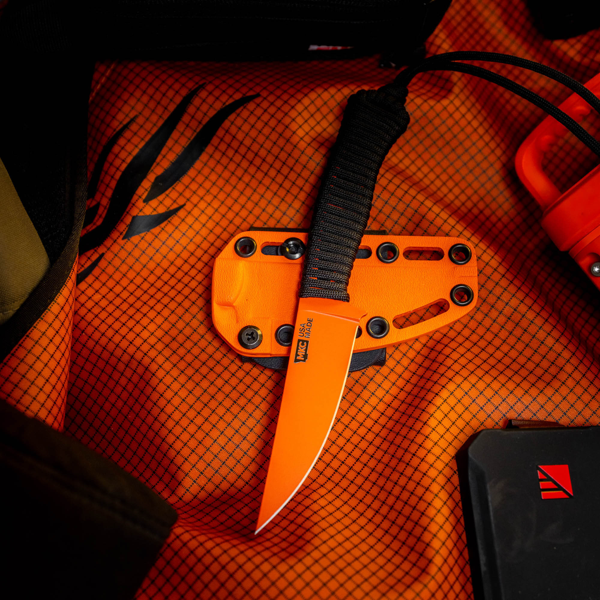 SPEEDGOAT 2.0 knife with blaze orange Cerakote finish resting on an orange mesh background, showcasing its tactical design.