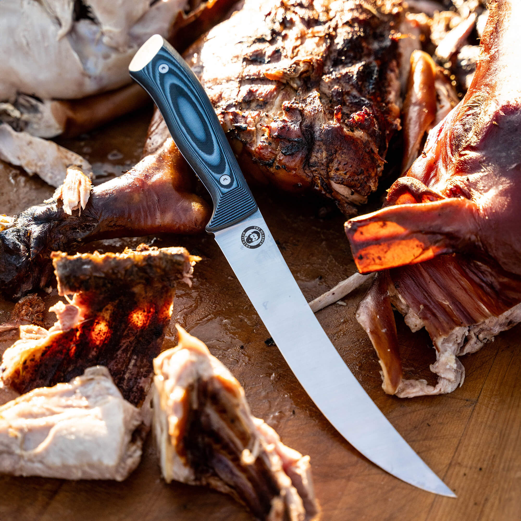 Alt Text: "Bearded Butchers Breaking Butcher knife prominently displayed next to a well-roasted, sliced assortment of meats, including ribs. The knife features a detailed, ergonomic handle and a clean, sharp blade, showcasing its high-quality craftsmanship ideal