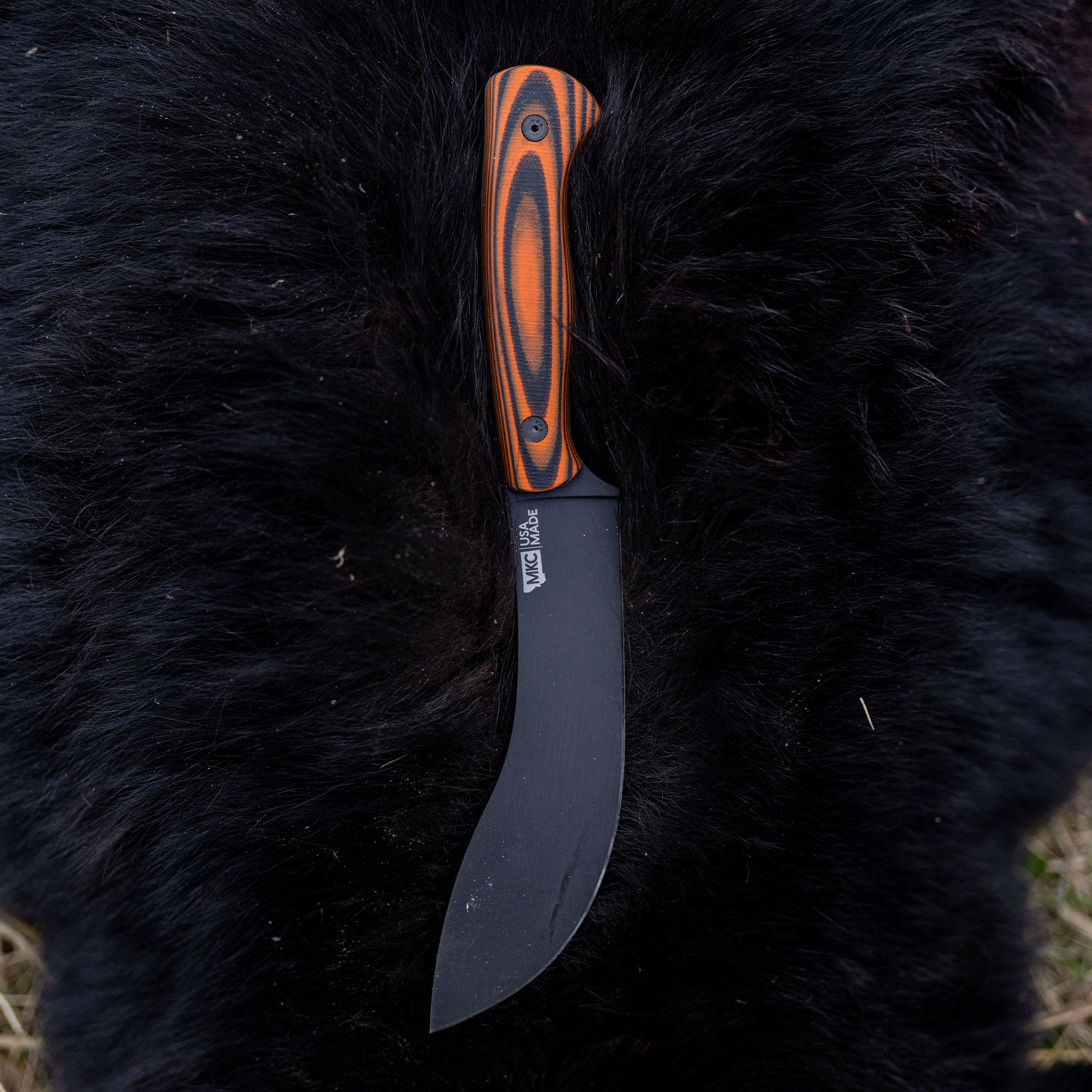 Orange and black Beartooth professional skinning knife with a curved blade, displayed on a black fur background.