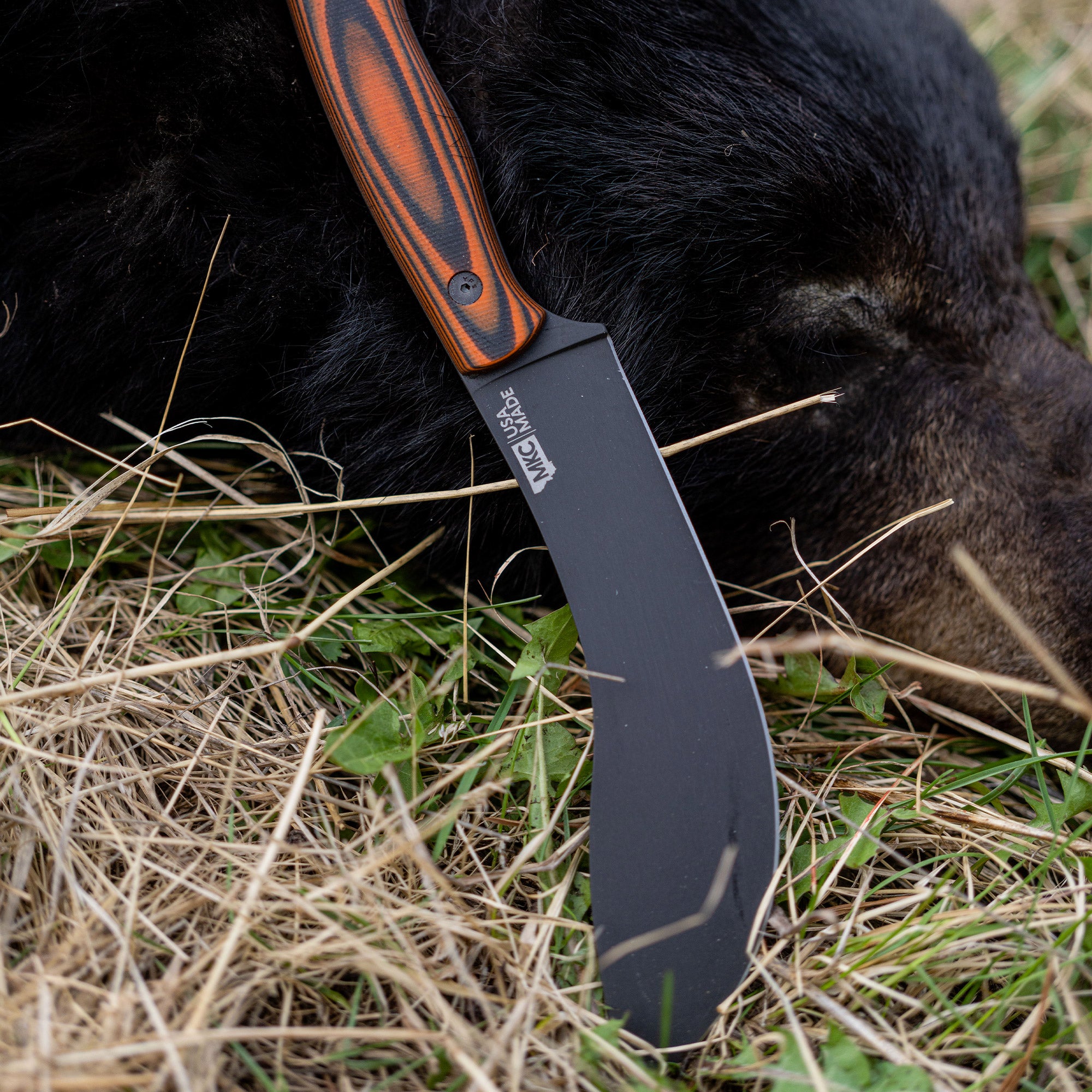 Orange and black Beartooth Pro Skinning Blade with a long, straight edge, resting on grass next to black fur.