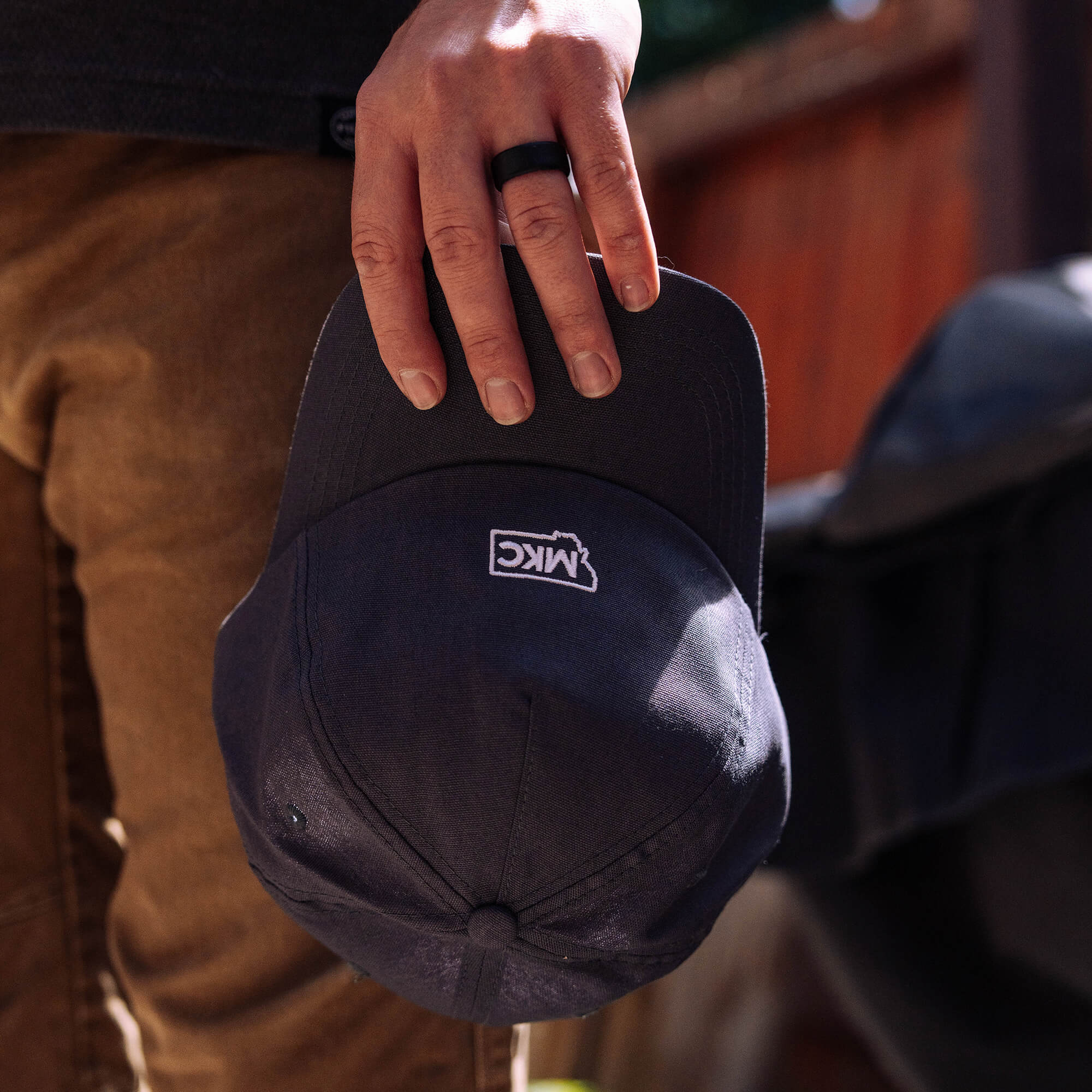 Grey MKC canvas dad hat held by a person, showcasing the logo on the underside of the brim. Ideal for outdoor enthusiasts.