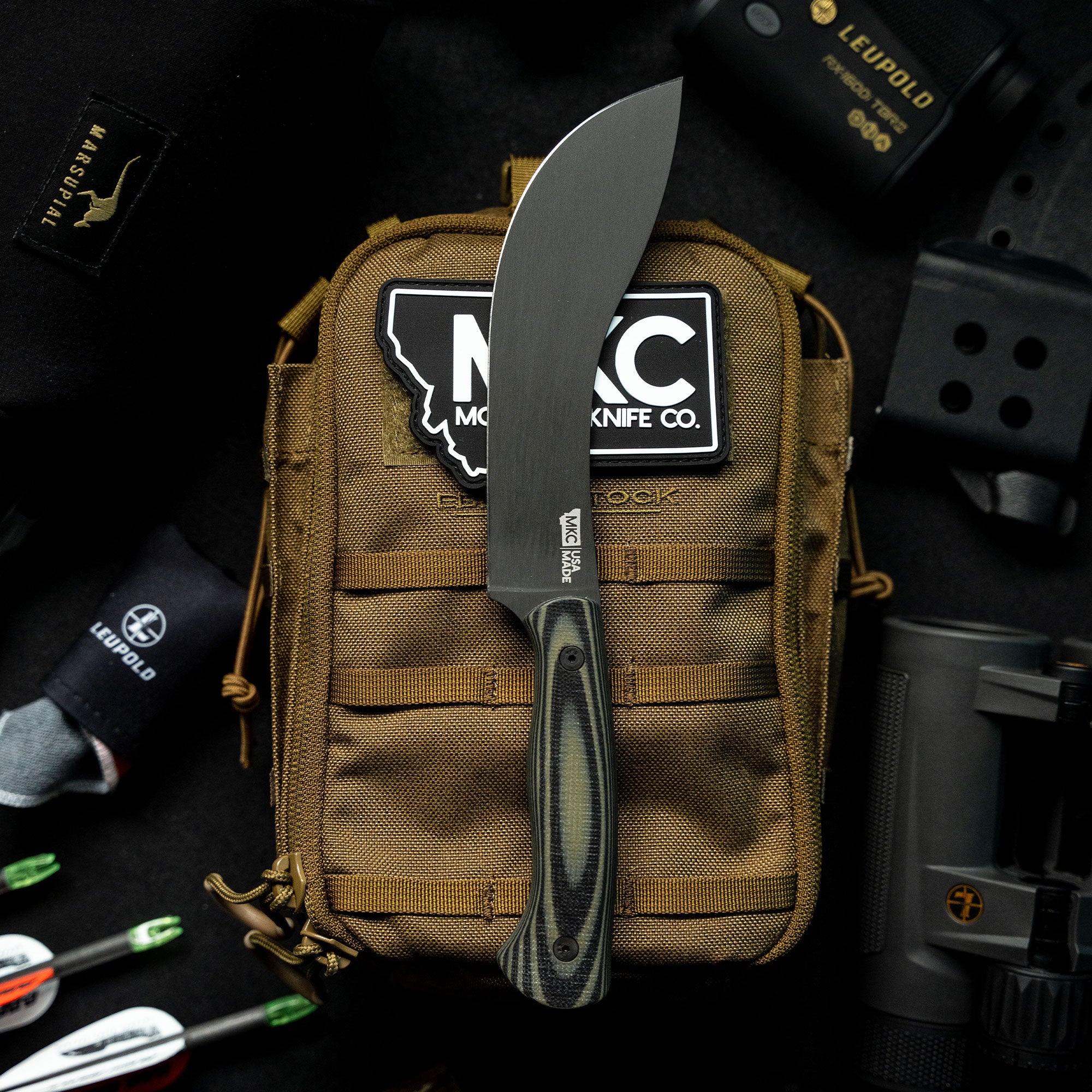 A Beartooth Pro Skinning Knife with a green and black handle prominently displayed on a tactical gear pouch, surrounded by outdoor and hunting equipment.