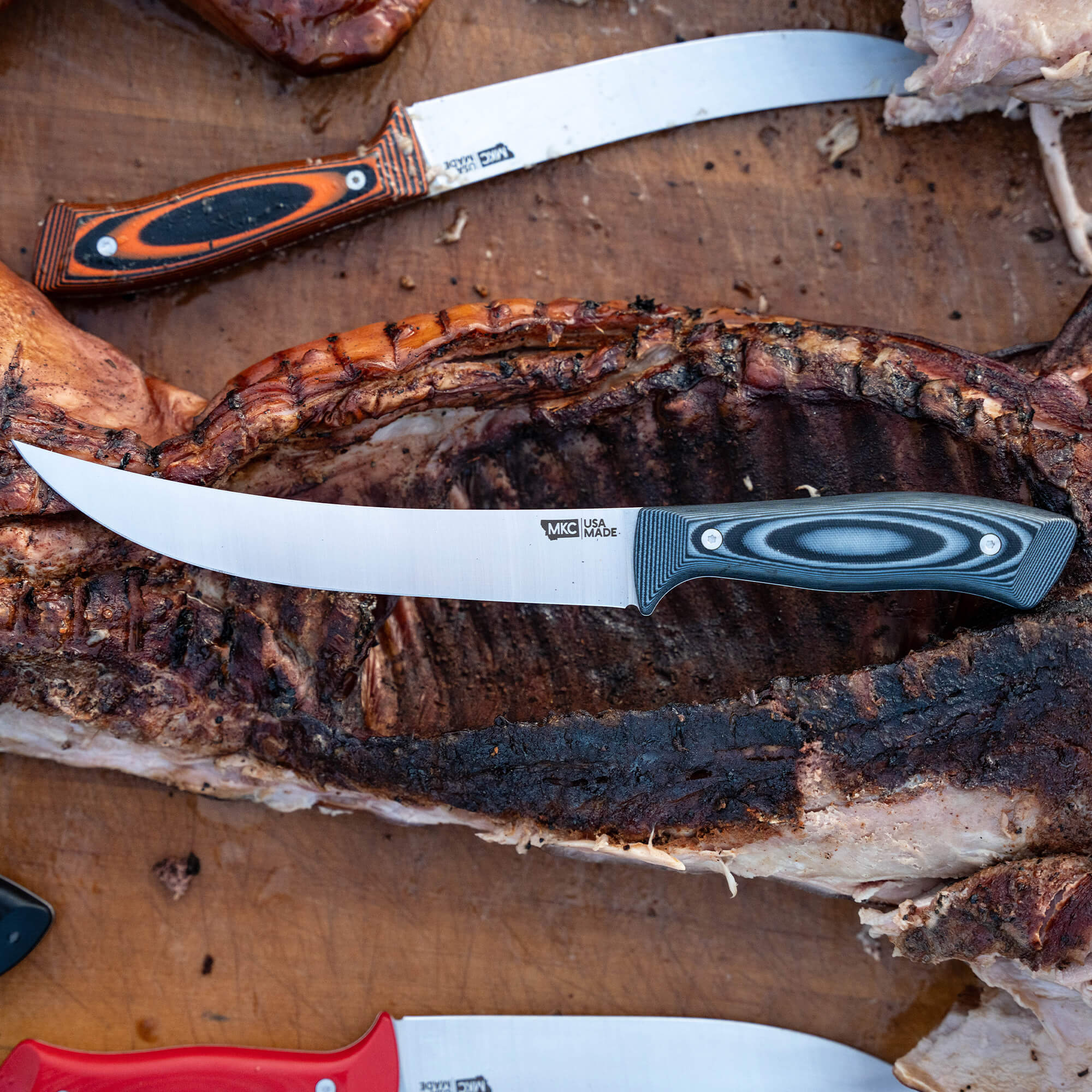 Two high-quality butchering knives with detailed handles laid next to a grilled rack of ribs on a wooden cutting board.