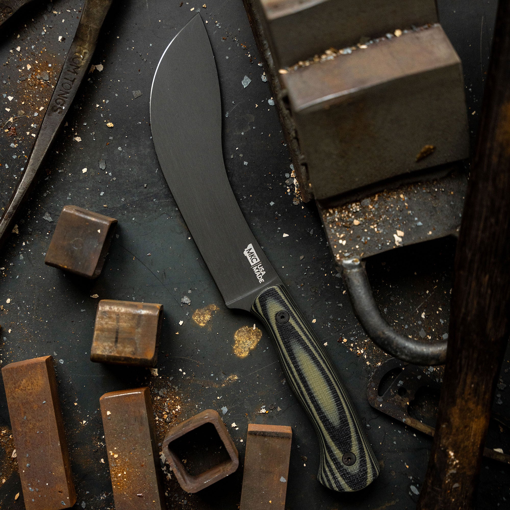 Alt text: "BEARTOOTH Pro Skinning Blade with a green and black handle, displayed on a gritty dark surface surrounded by metal chunks and dust, highlighting the knife's matte black blade and rugged design."