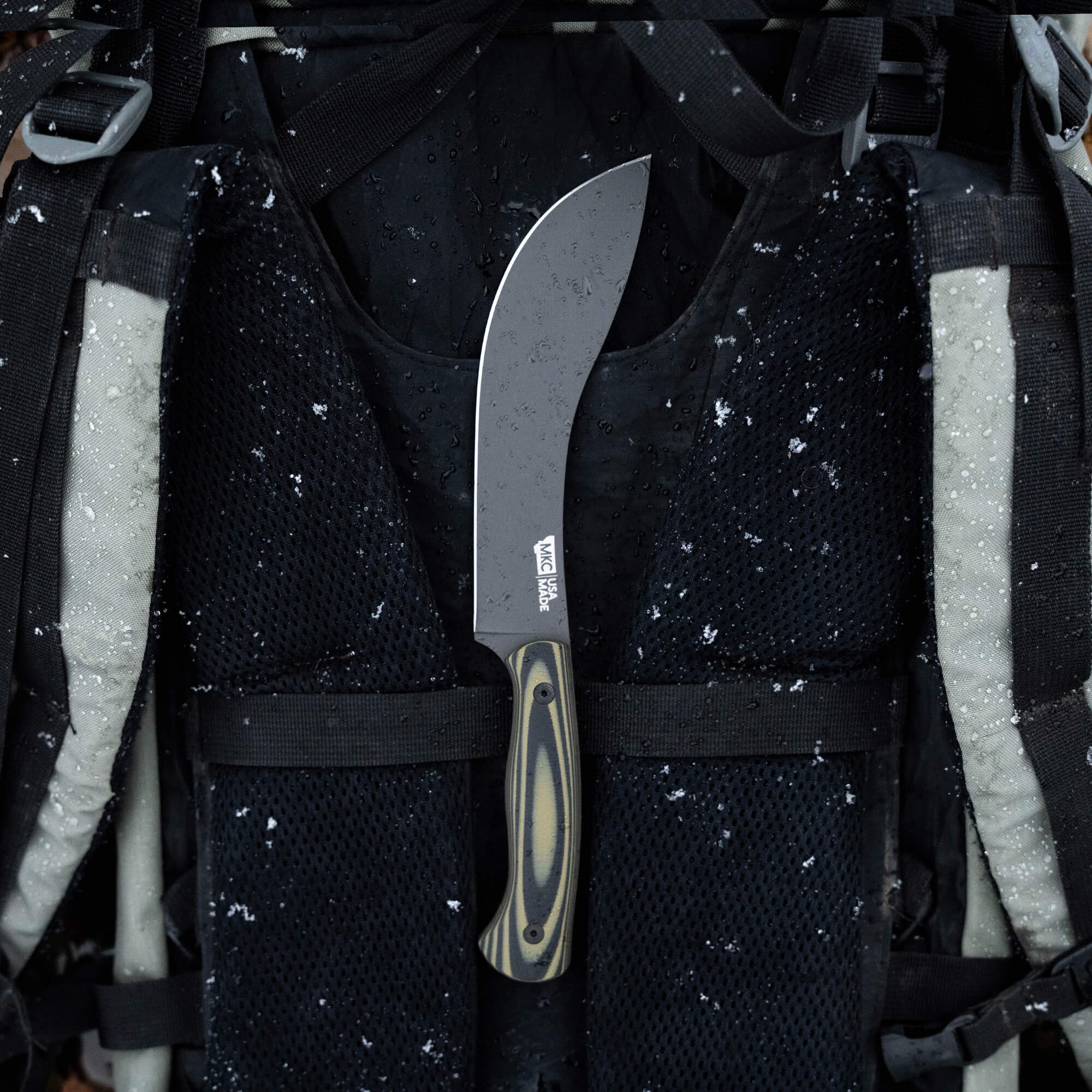 Alt text: "Beartooth Pro Skinning Blade with a green and black handle secured vertically in a tactical vest covered with raindrops, focusing on the durability and design of the knife ideal for outdoor use."