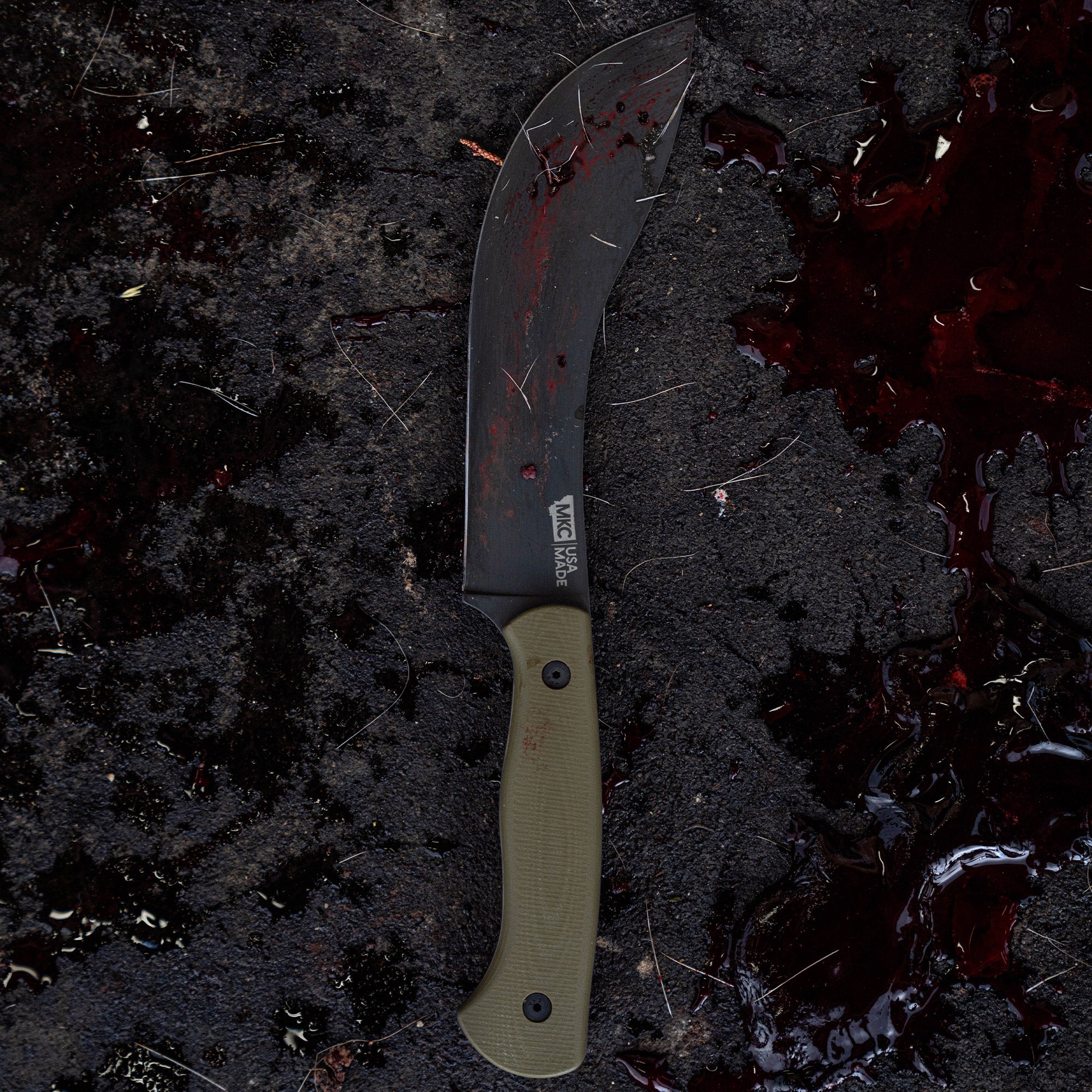 Alt text: "Beartooth Pro Skinning Blade in olive color with curved blade and ergonomic handle, showcased on a dark, muddy surface with visible blood stains."