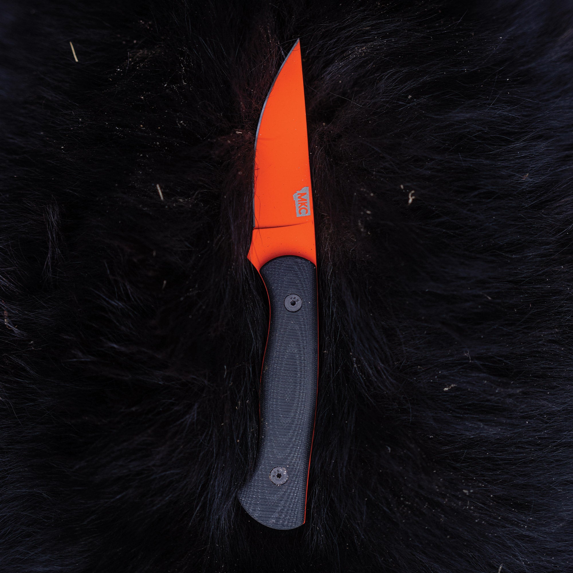 Alt text: "BLACKFOOT 2.0 knife with a blaze orange Cerakote blade and black handle, displayed against a dark fur background."