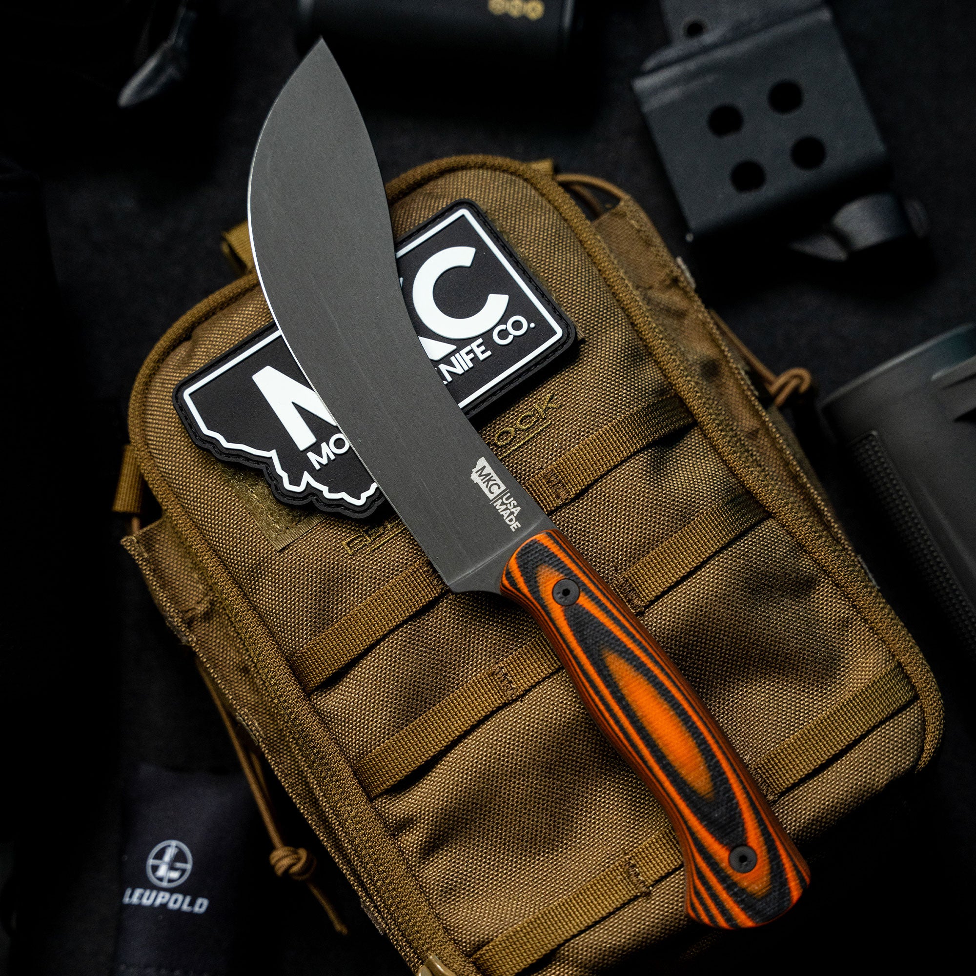 Alt text: "Beartooth Pro Skinning Blade with an orange and black handle, displayed on a brown tactical bag, featuring sharp, straight-edge blade design suitable for precise skinning tasks."