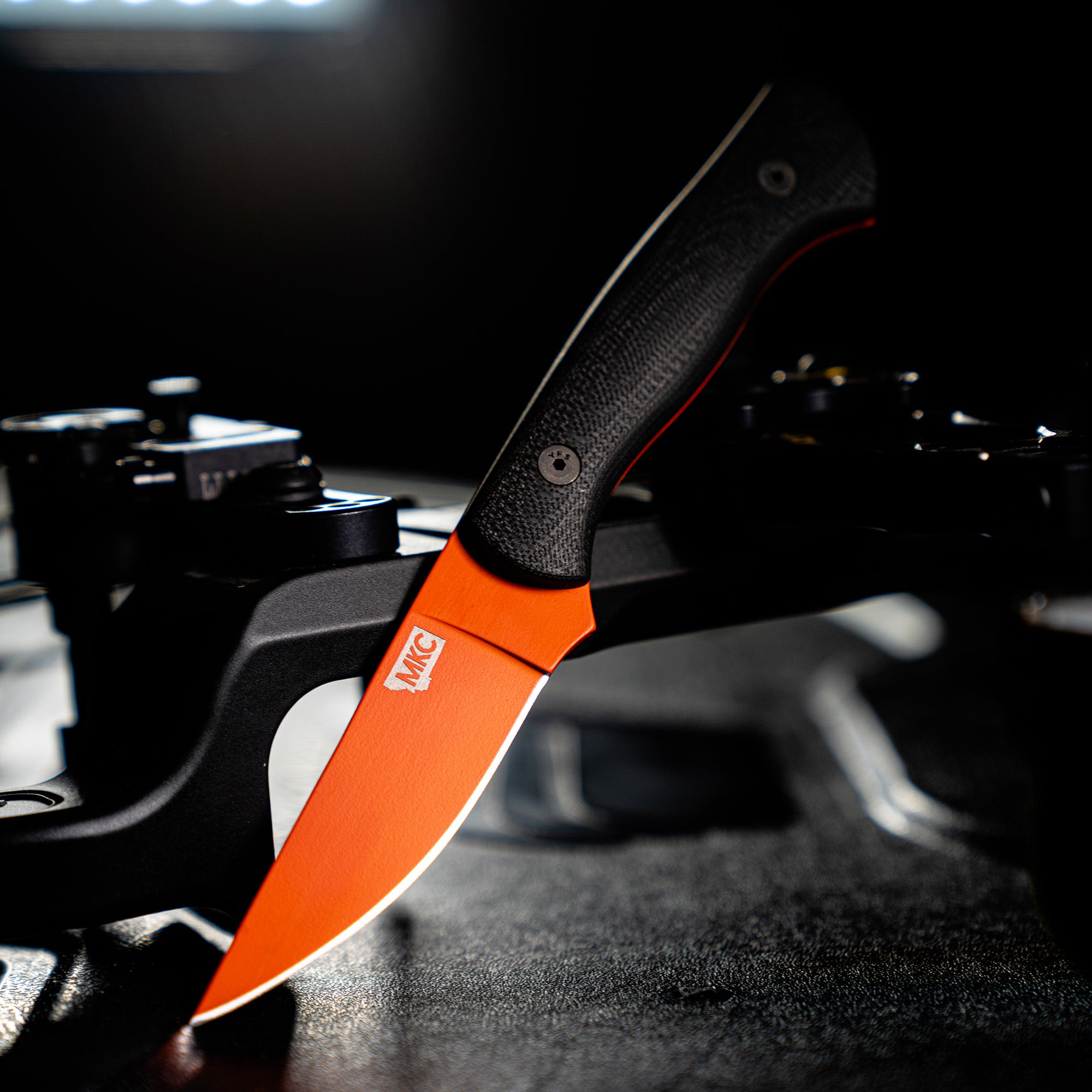 Alt text: "Close-up of the BLACKFOOT 2.0 knife with Blaze Orange Cerakote™ blade, featuring a textured black handle. The knife is prominently displayed against a dark, blurred background with soft lighting highlighting its sleek design."