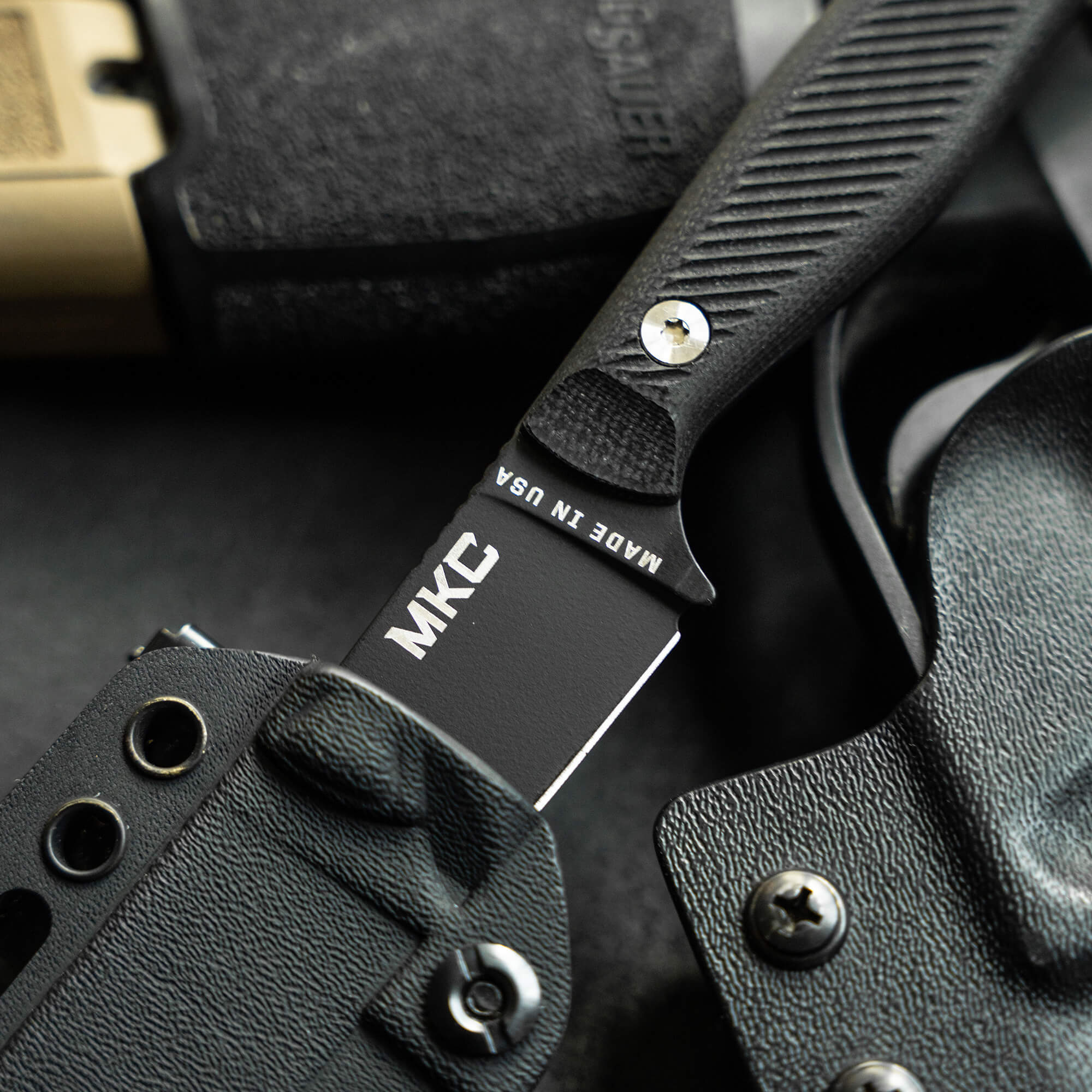 Close-up image of the MKC Battle Goat tactical knife in black, featuring a prominent branding on its black blade, textured handle for grip, and a custom sheath.