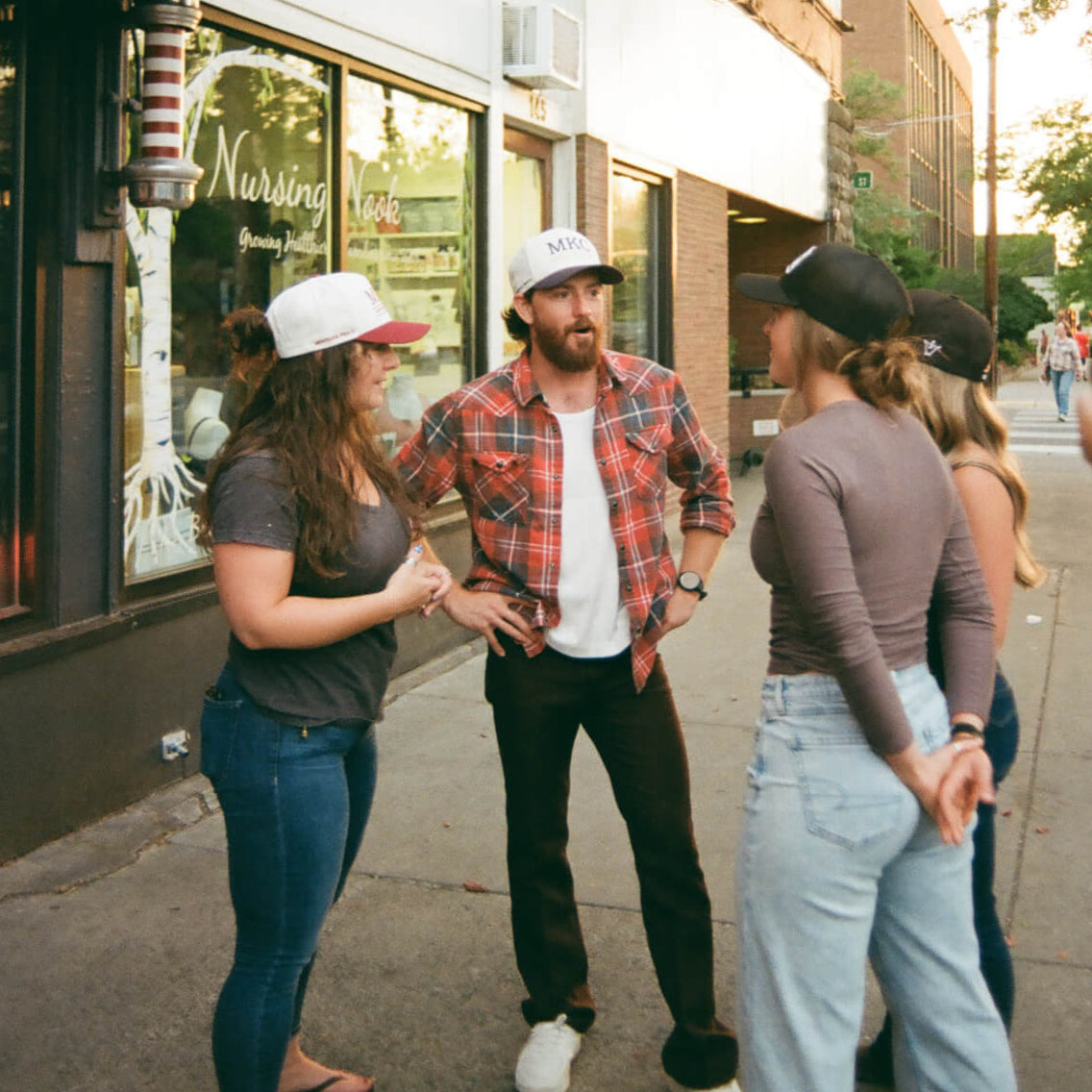 Group of people standing on a sidewalk in front of a store with a person taking a photo.