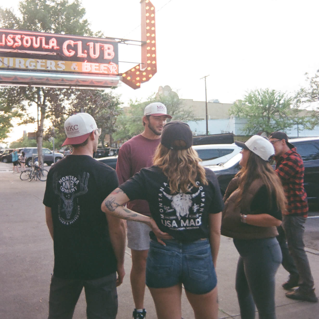 Group of people standing outside a building with a sign that reads 'Missoula Club'.