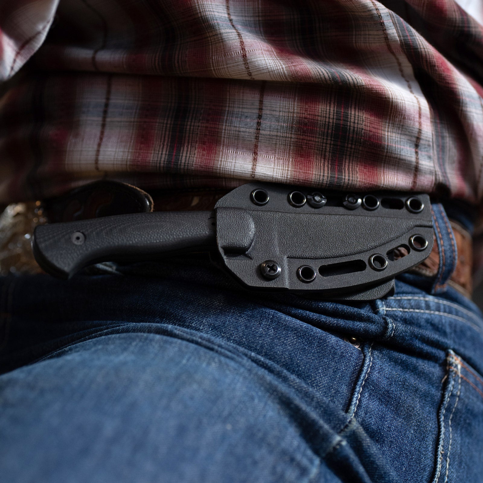 Alt Text: "Close-up view of a Blackfoot 2.0 tactical knife in black, clipped into the pocket of a person wearing denim jeans and a plaid shirt."