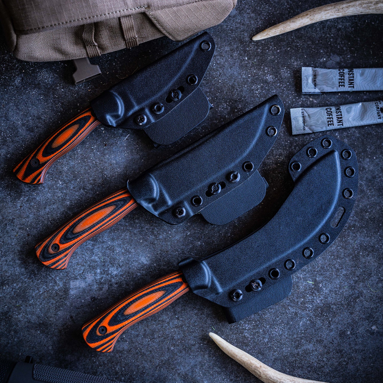 Alt text: "Array of Beartooth professional skinning knives with orange and black handles, displayed with their black sheaths on a textured grey surface, accompanied by hunting gear elements."