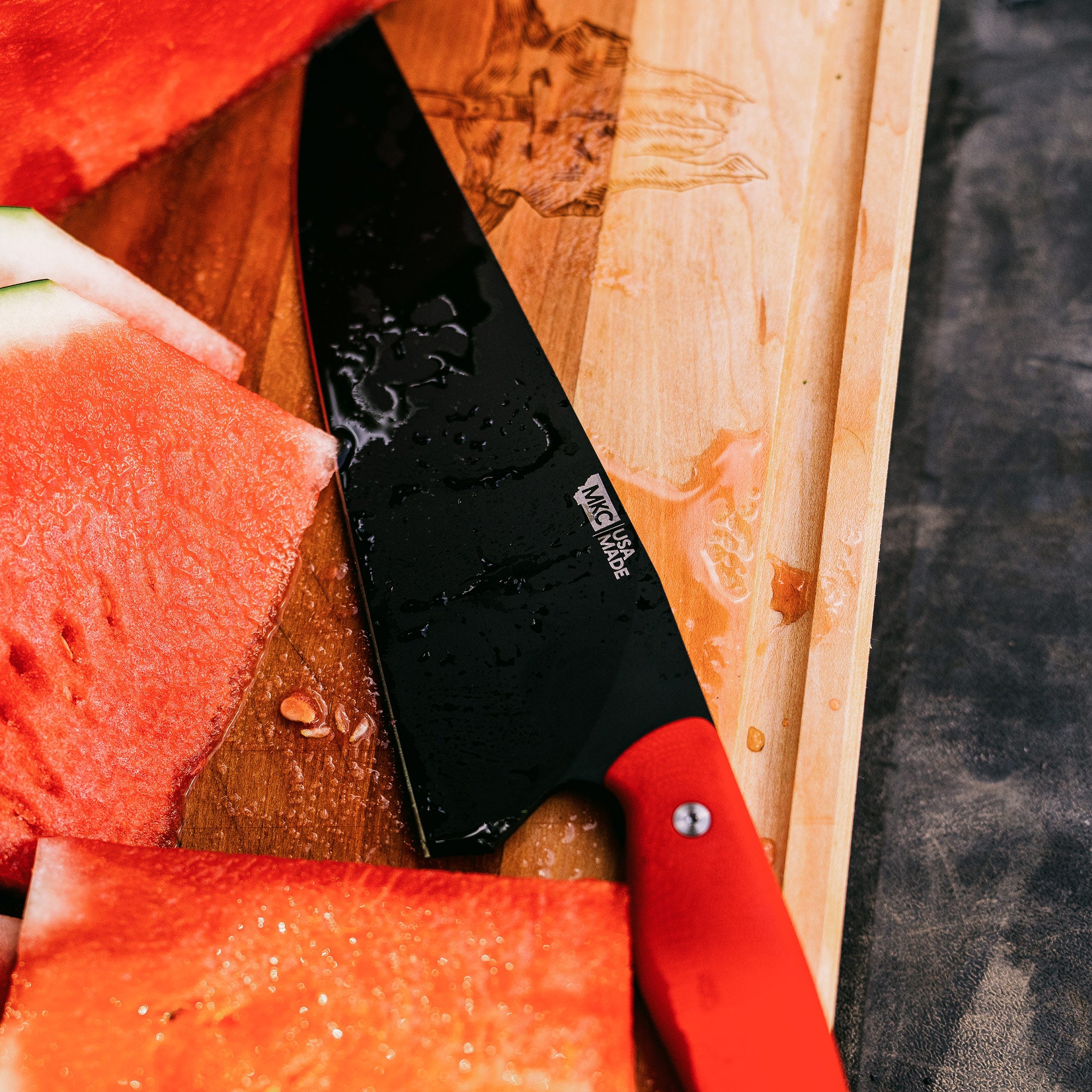 "Close-up image of a Bighorn Chef knife with a red handle, cutting through watermelon slices on a wooden cutting board."