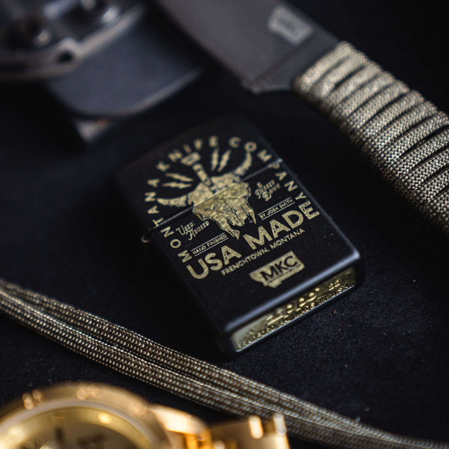 Black Zippo lighter featuring a gold-tone Bison skull design and “USA Made” text, presented on a dark background with a pocket knife and watch, emphasizing its rugged aesthetic.