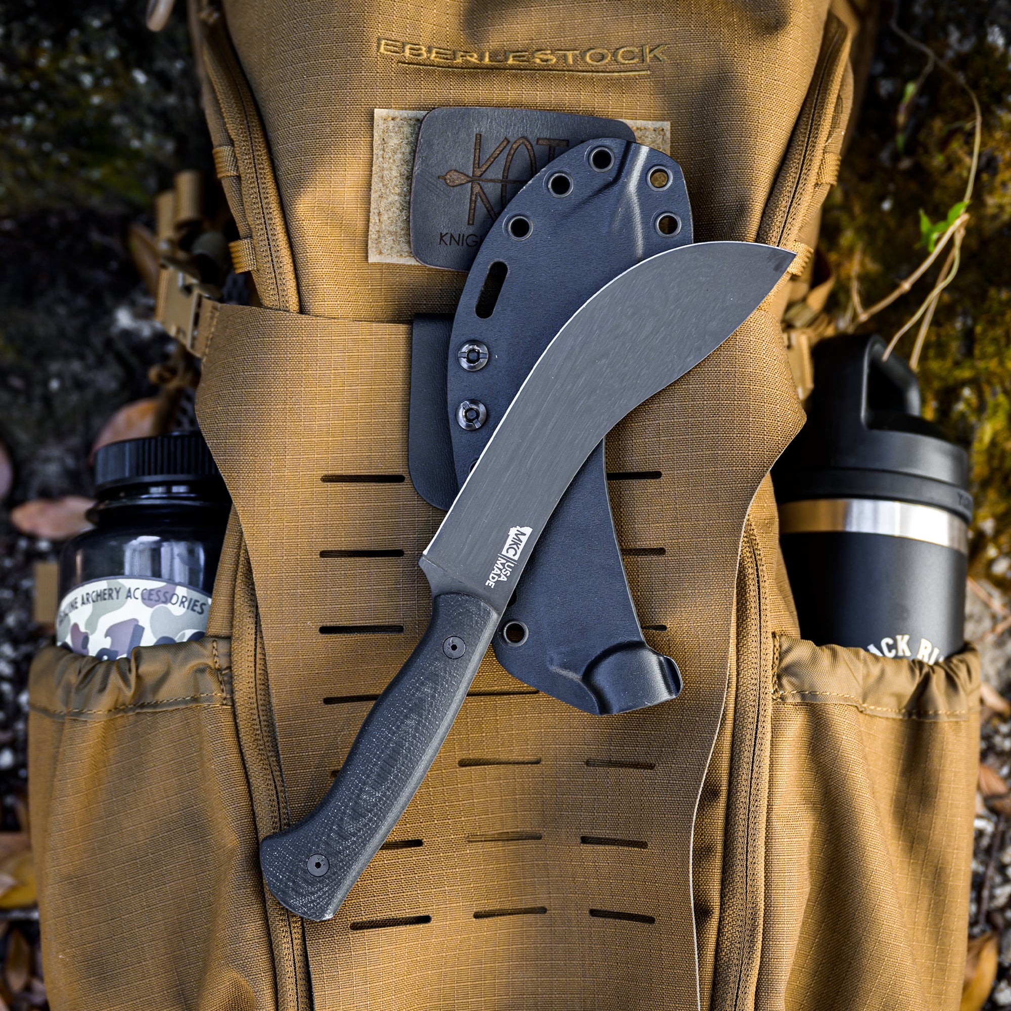 Alt text: "A Beartooth Pro Skinning Blade with a curved black blade and textured handle, displayed on a khaki-colored hunting vest alongside other outdoor gear."