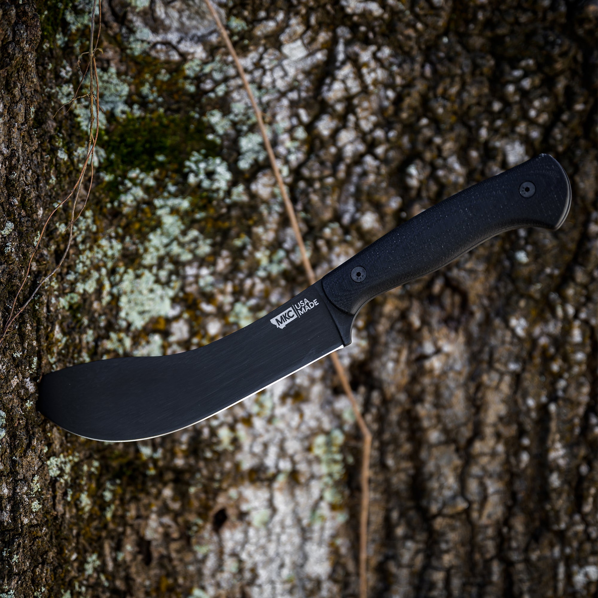 Black Beartooth Pro Skinning blade with ergonomic handle, displayed against a textured tree bark background.