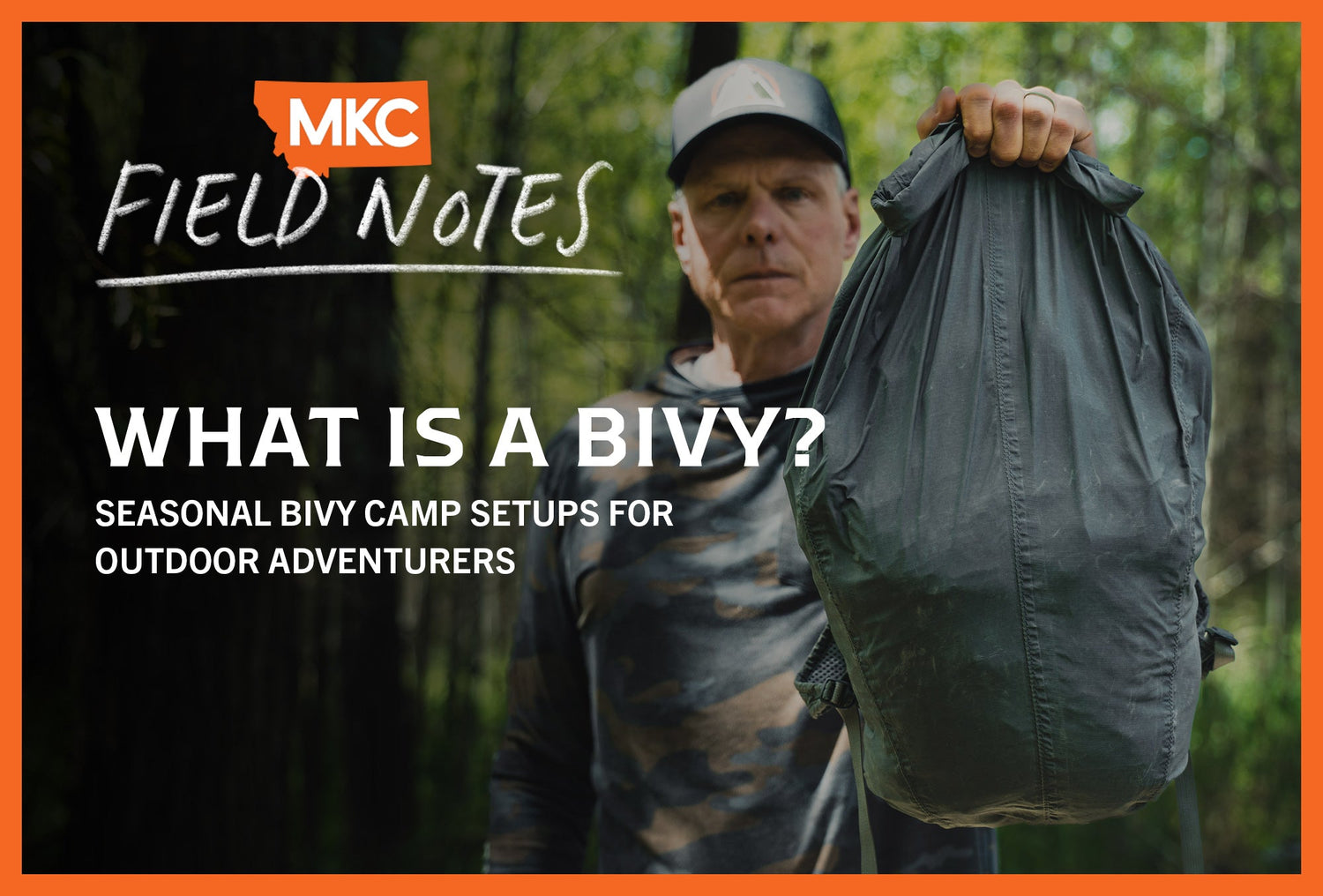 Man standing in a wooded area holding a compact bivy sack, preparing for a minimalist overnight camp.