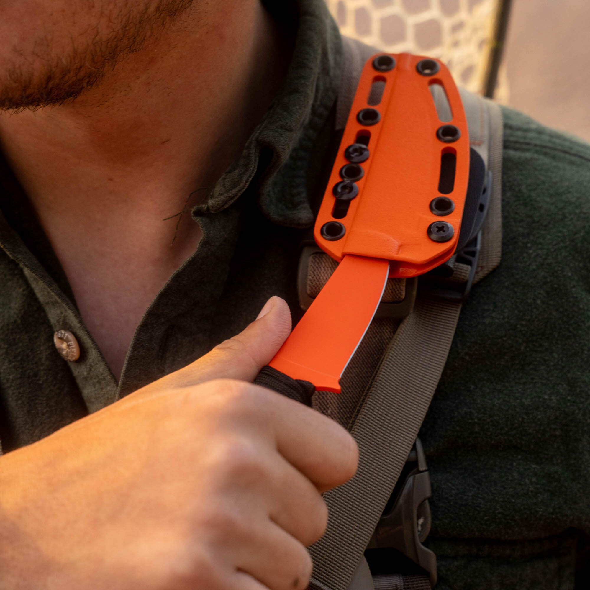 Blaze orange SPEEDGOAT 2.0 knife secured on a shoulder strap, showcasing its durable design and functionality.