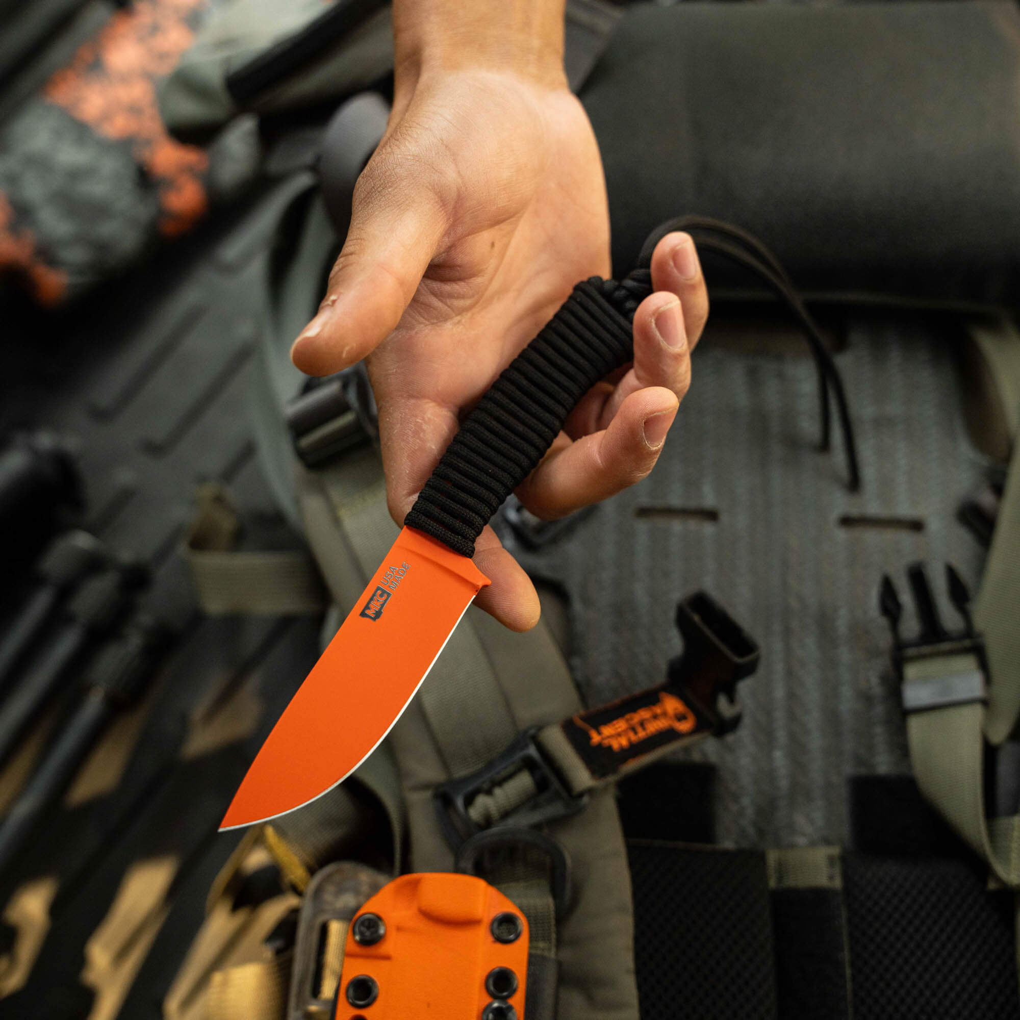Blaze orange Cerakote STONED GOAT 2.0 knife held in a hand, showcasing its durable blade and textured grip.