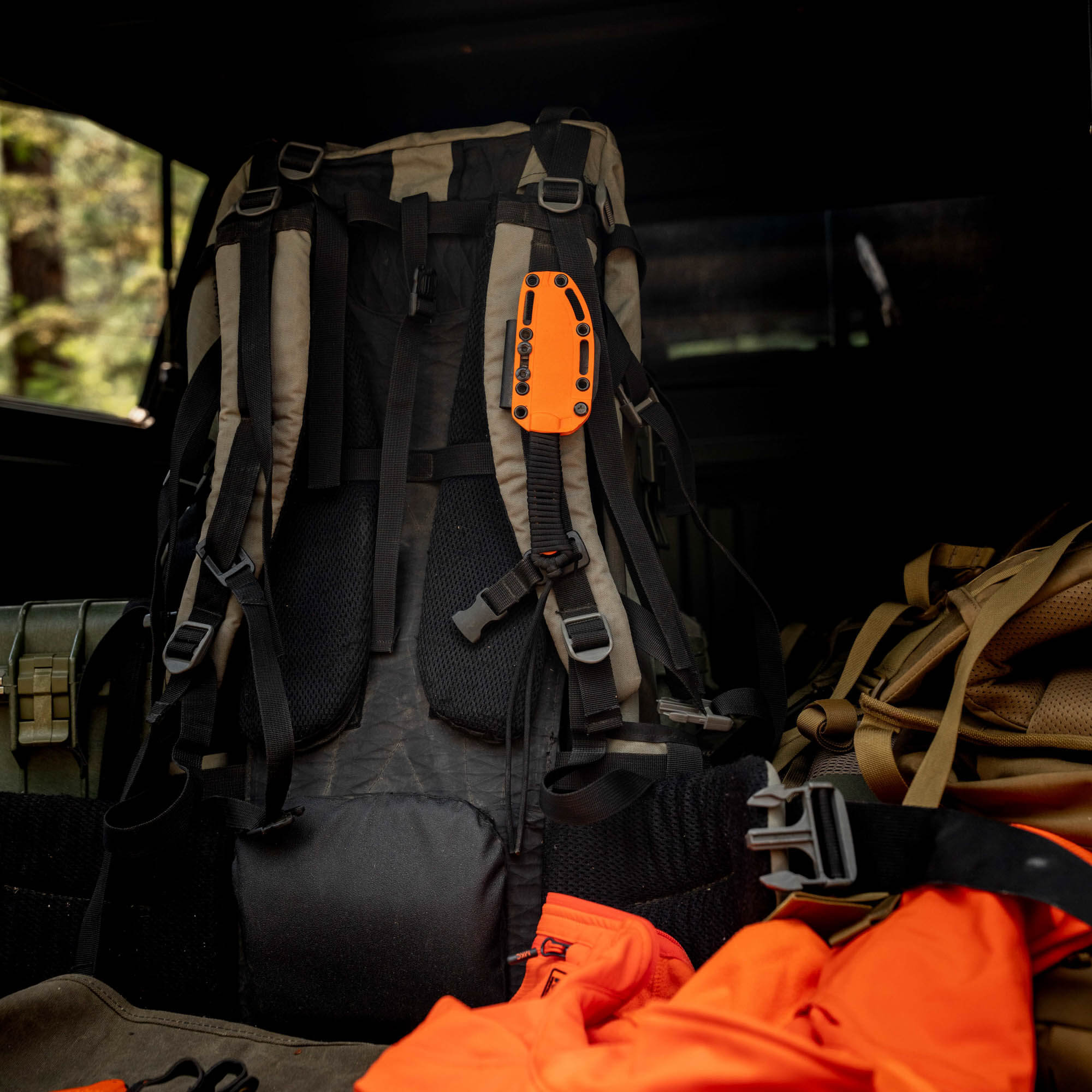 Blaze orange STONED GOAT 2.0 knife on a backpack, showcasing its durable design for outdoor enthusiasts.
