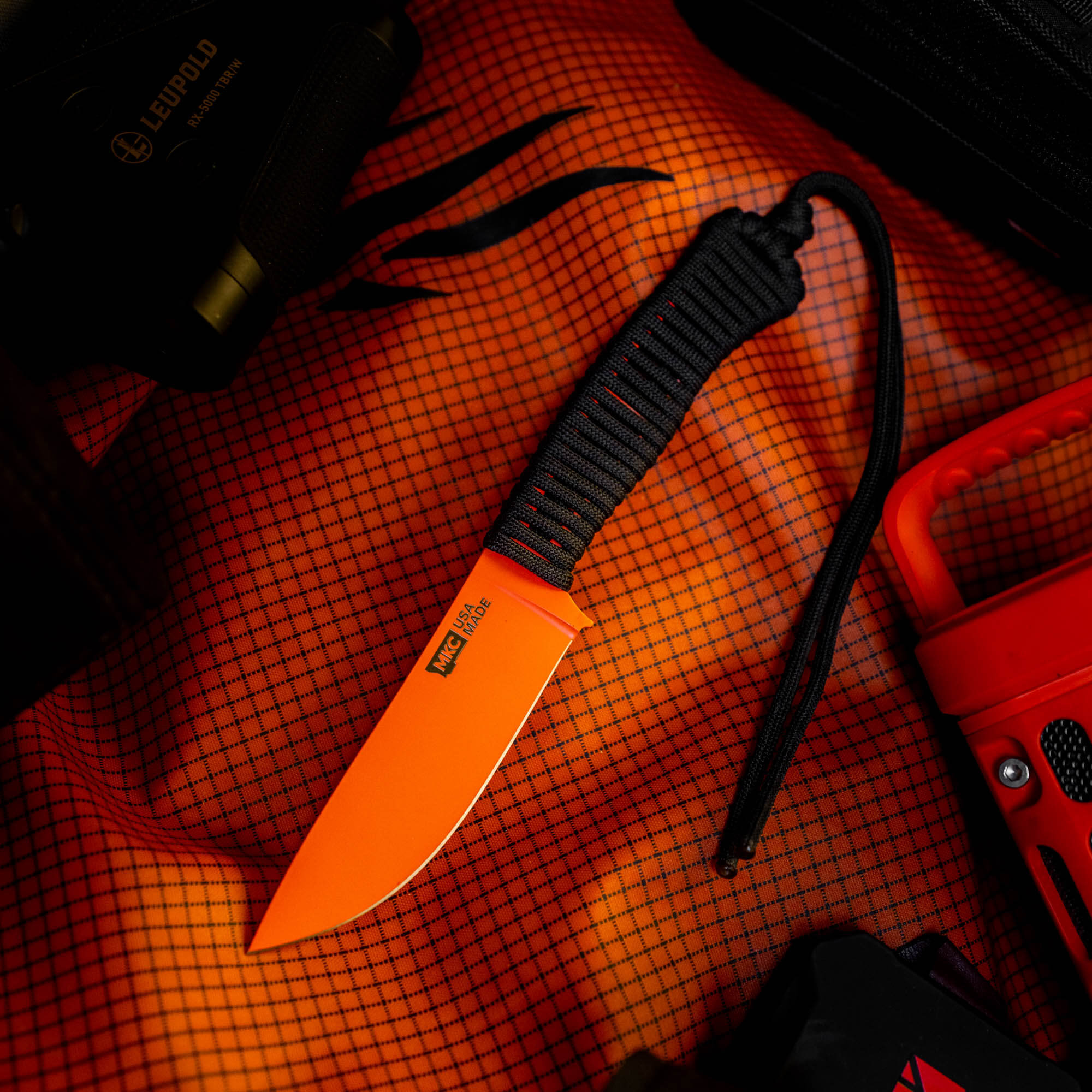 Blaze orange Cerakote knife with a black paracord handle, set against an orange patterned background. Ideal for outdoor use.