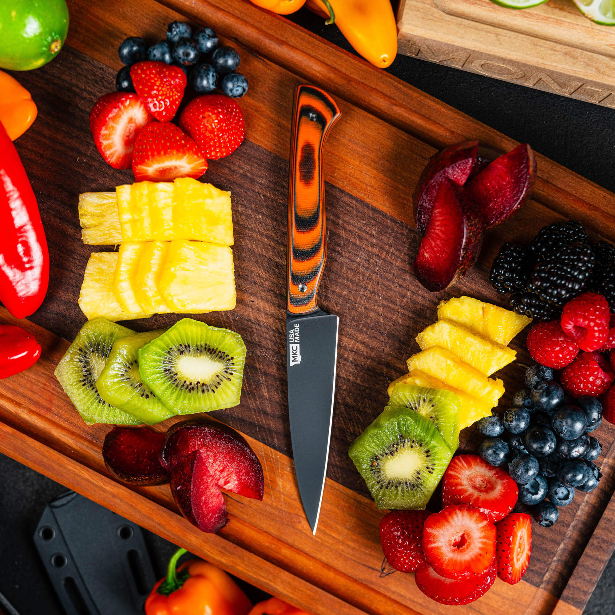 Montana Knife Company's Cutbank Paring Knife in orange and black, surrounded by fresh fruits and vegetables on a wooden cutting board.