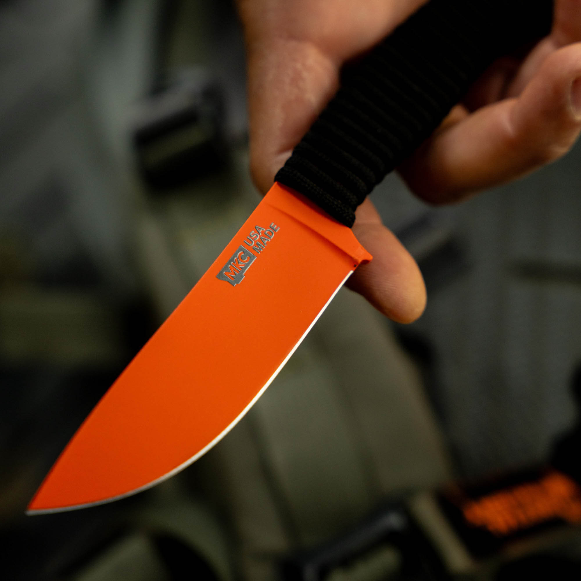 Blaze orange Cerakote knife with a black handle, designed for outdoor use and durability.
