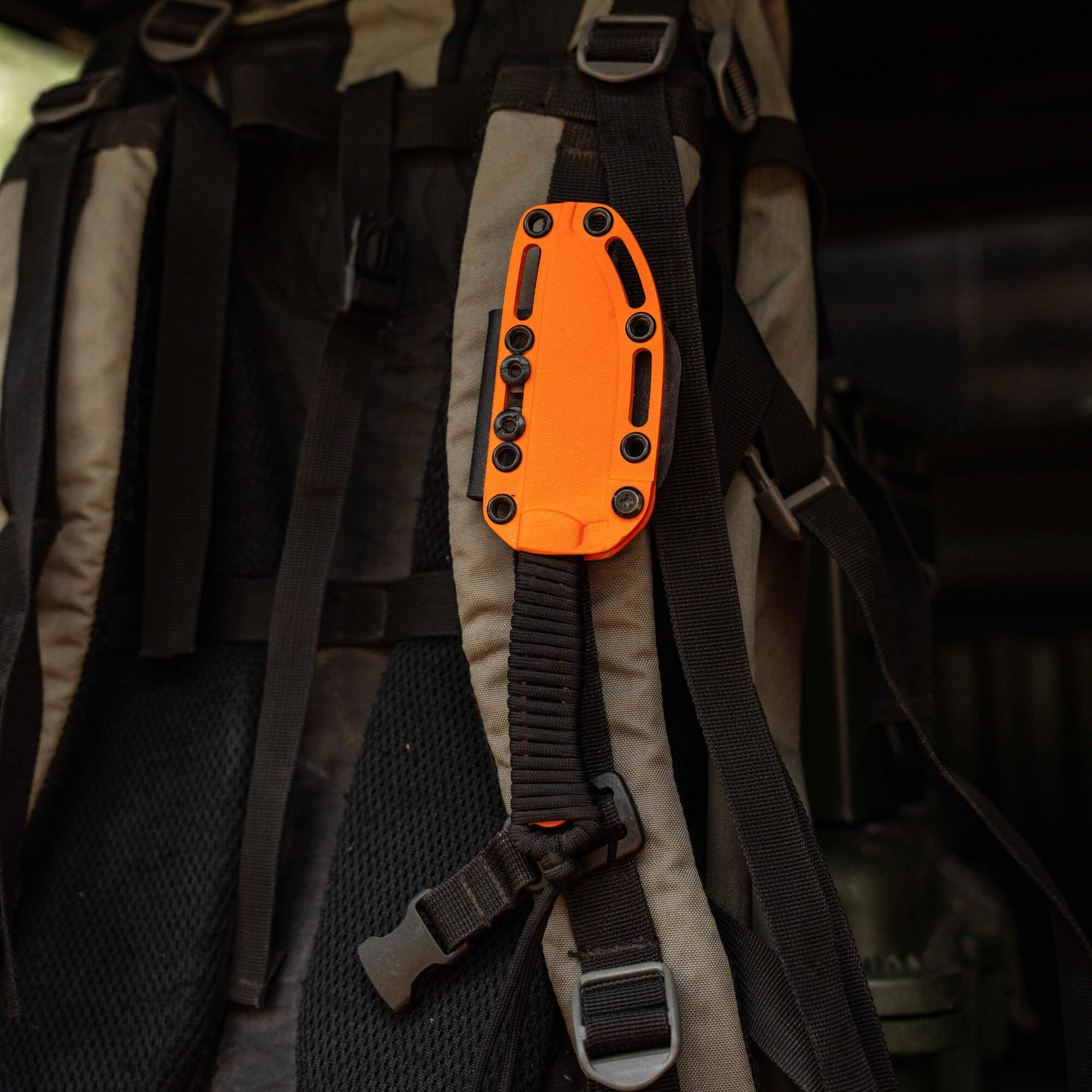 Blaze orange Cerakote STONED GOAT 2.0 knife sheath attached to a backpack strap, showcasing durability and visibility.