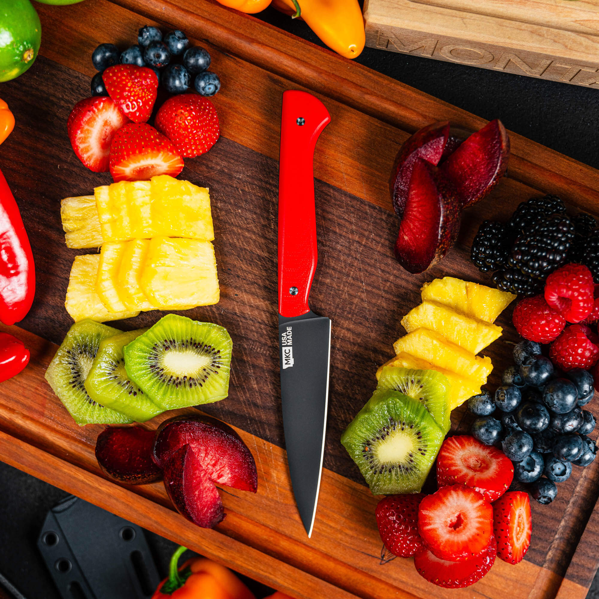 Montana Knife Company's Cutbank Paring Knife in red surrounded by fresh fruits and vegetables on a wooden cutting board.
