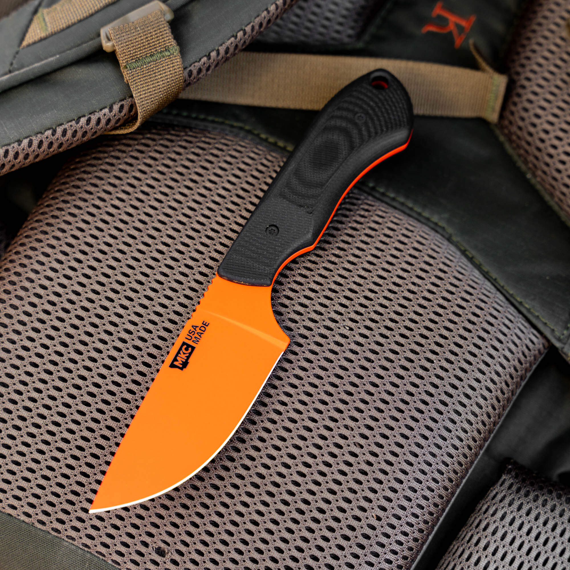 MKC Elk Knife with Blaze Orange Cerakote finish, featuring a durable black handle, resting on a textured surface.