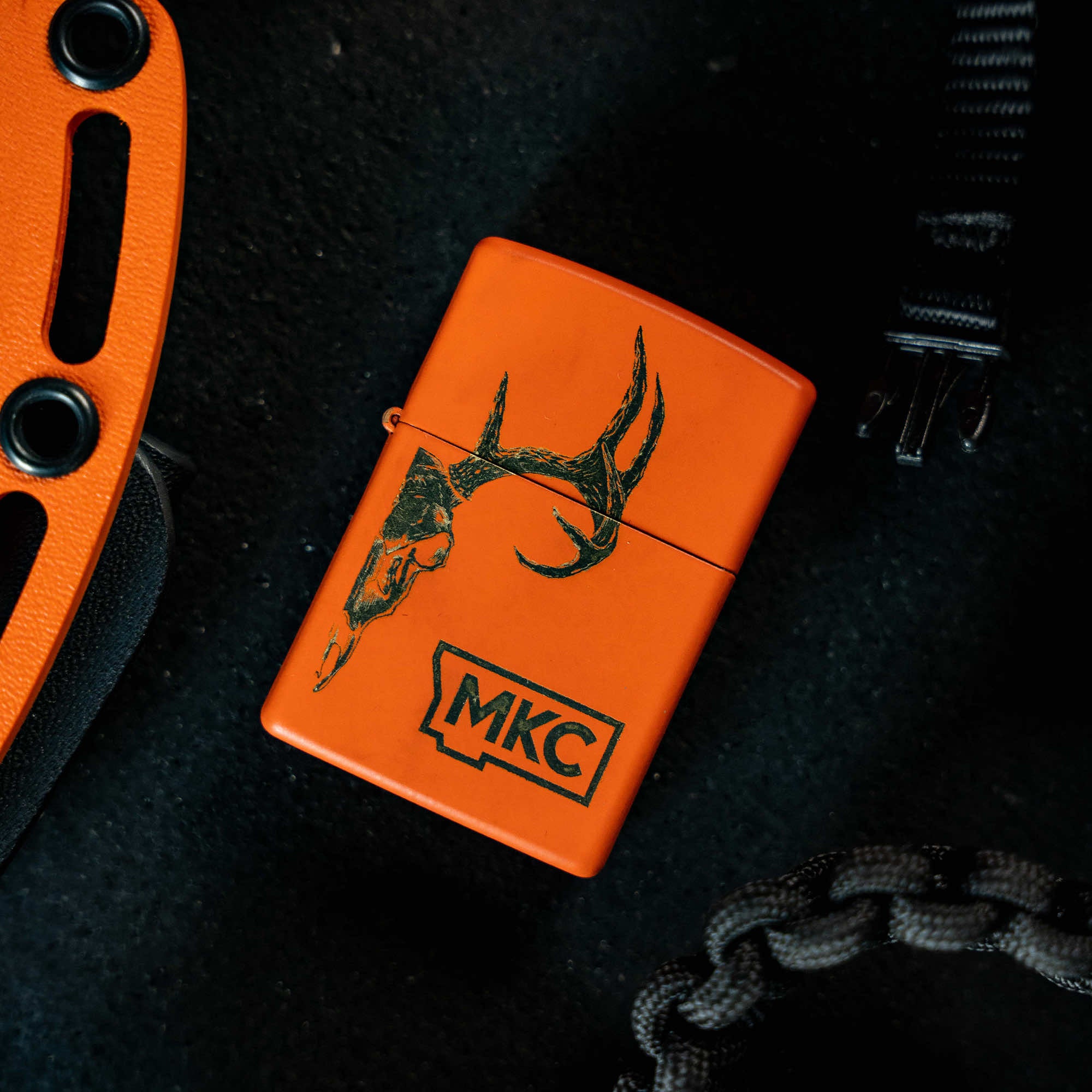 Limited edition blaze orange Zippo lighter with MKC logo and deer antler design, made in the USA. Ideal for outdoor enthusiasts.