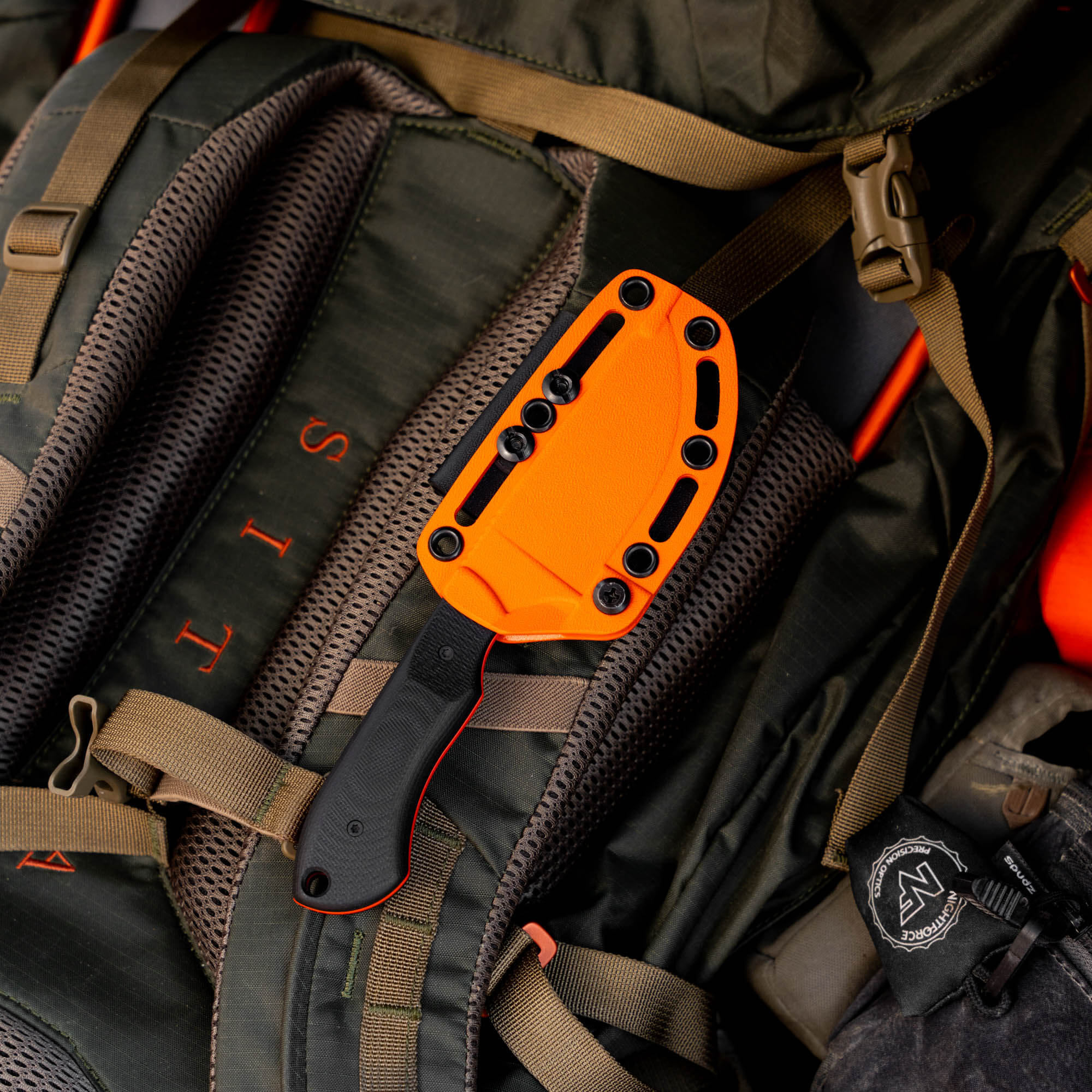 MKC Elk Knife with Blaze Orange Cerakote resting on a tactical backpack, showcasing its durable design for outdoor use.