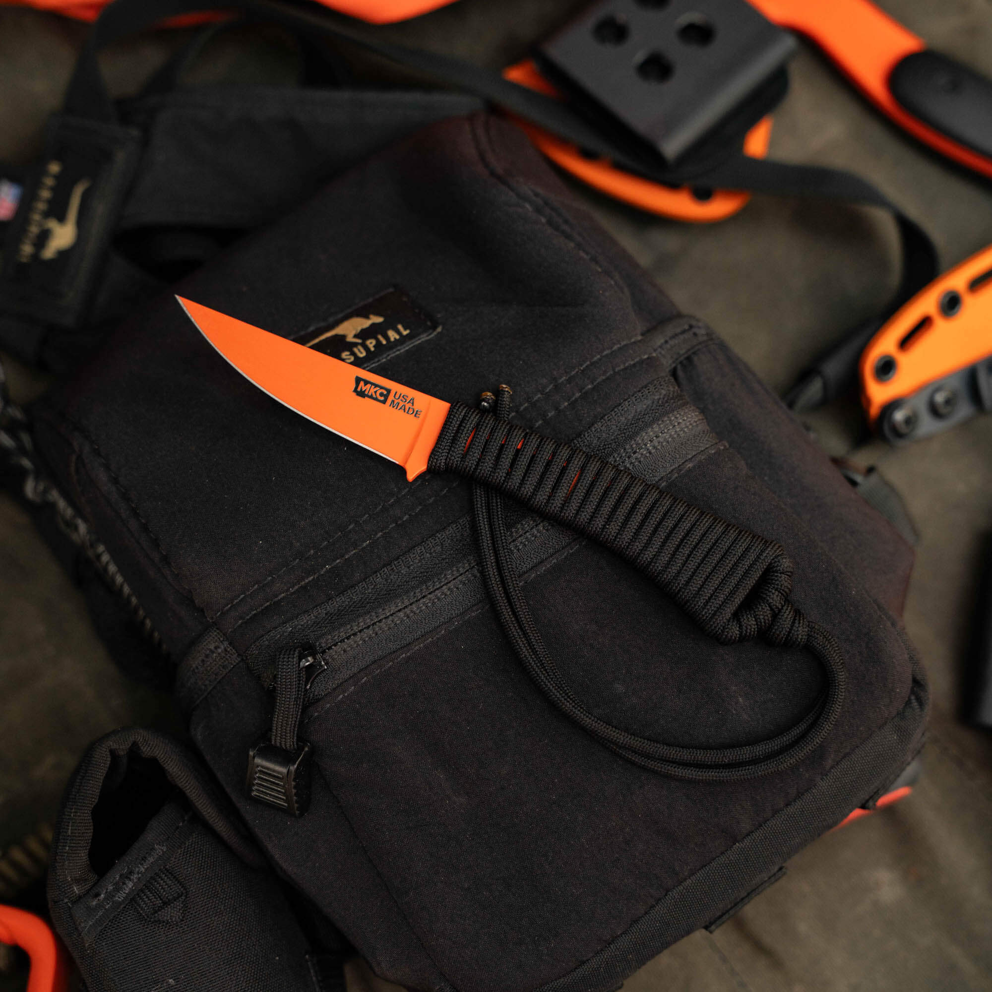 Mini Speedgoat 2.0 knife with blaze orange Cerakote finish on a black backpack, showcasing its compact design and functionality.