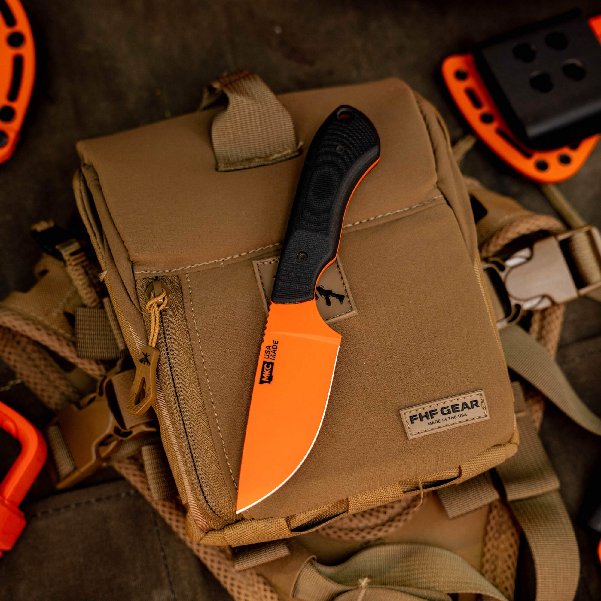 MKC Elk Knife in Blaze Orange Cerakote with a black handle, resting on a tactical bag, ideal for outdoor use.