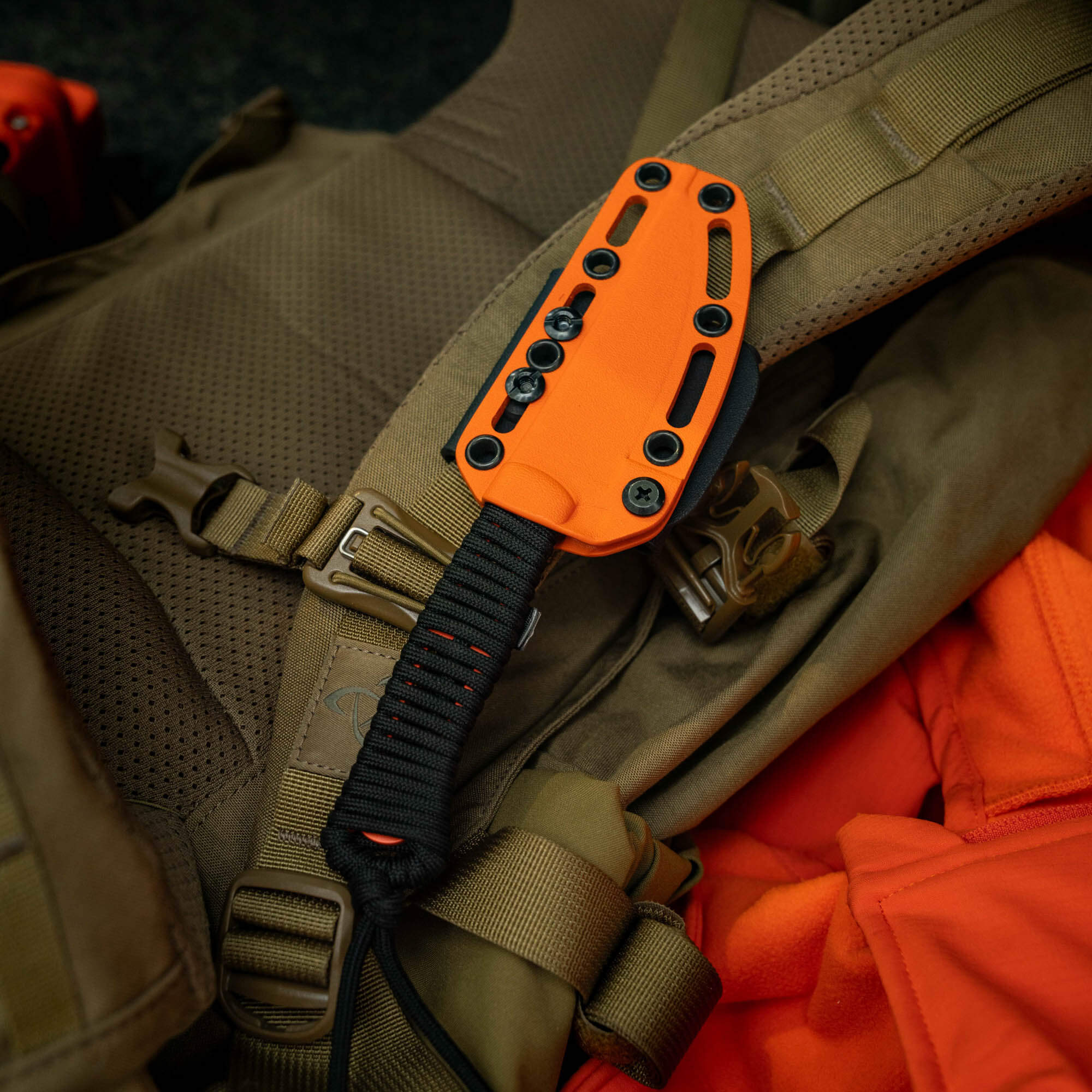SPEEDGOAT 2.0 knife with blaze orange Cerakote sheath resting on a tactical backpack, showcasing durability and visibility.