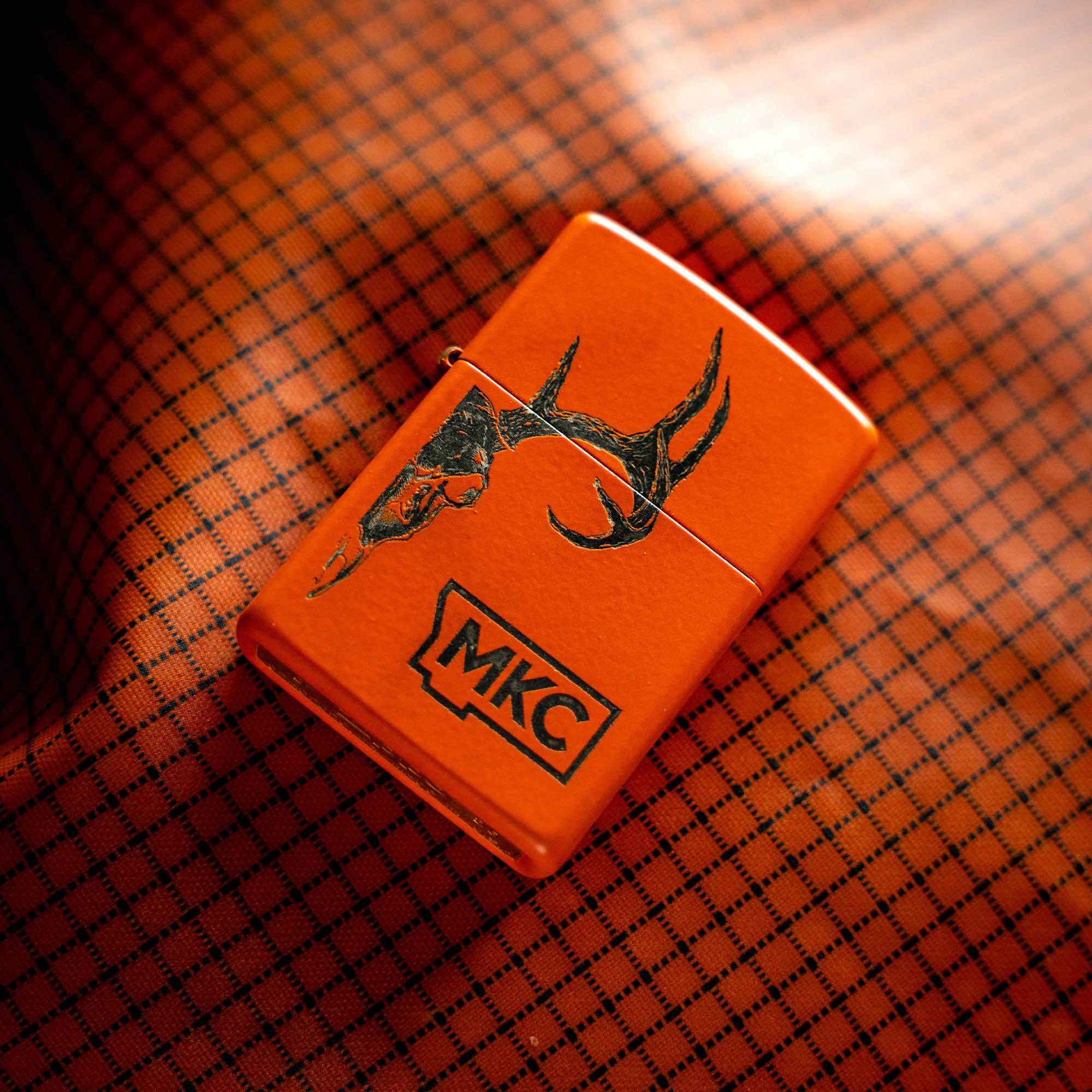 Limited edition blaze orange Zippo lighter with MKC logo and antler design, made in the USA. Perfect for outdoor enthusiasts.