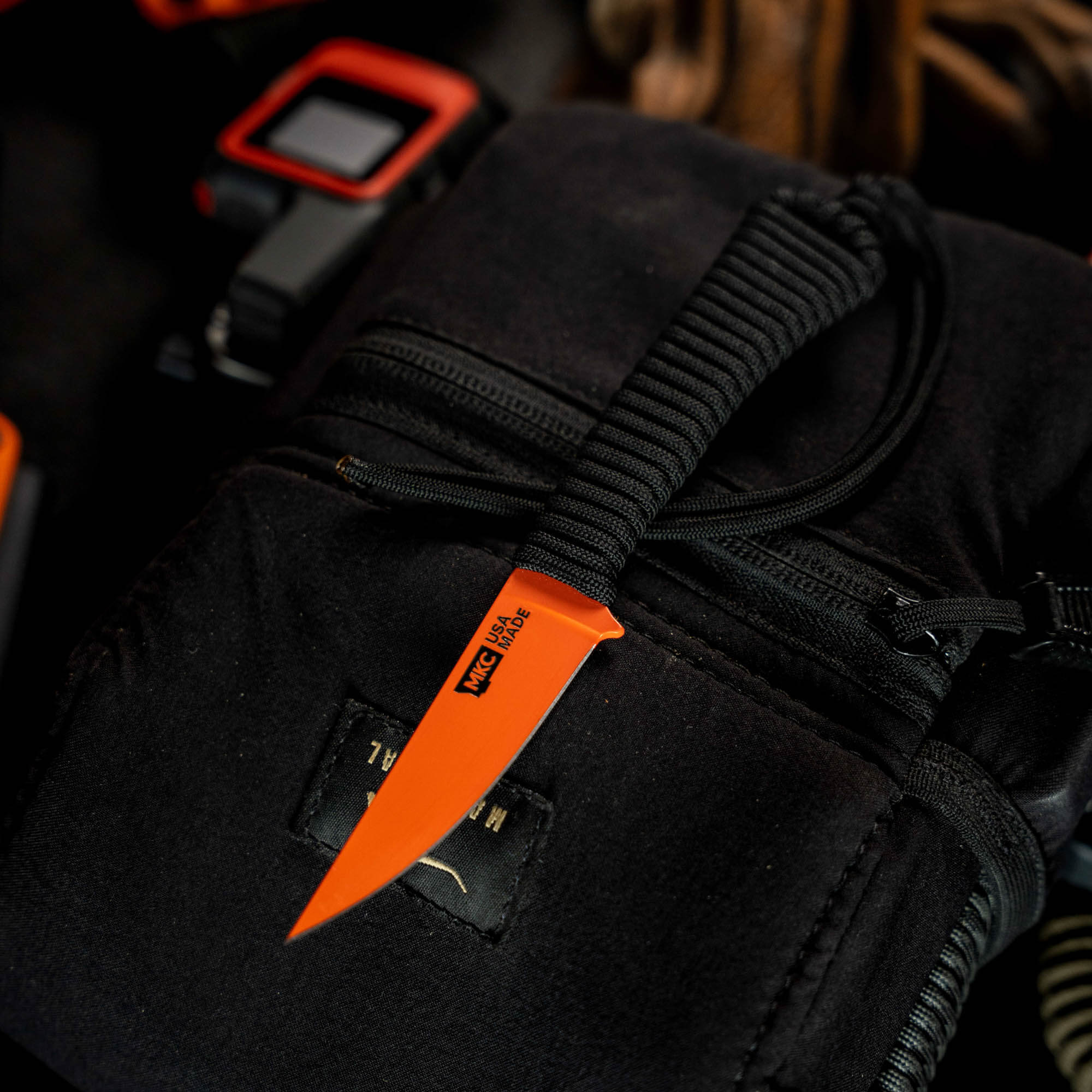Mini Speedgoat 2.0 knife with Blaze Orange Cerakote finish, resting on a black tactical pouch, ideal for outdoor use.
