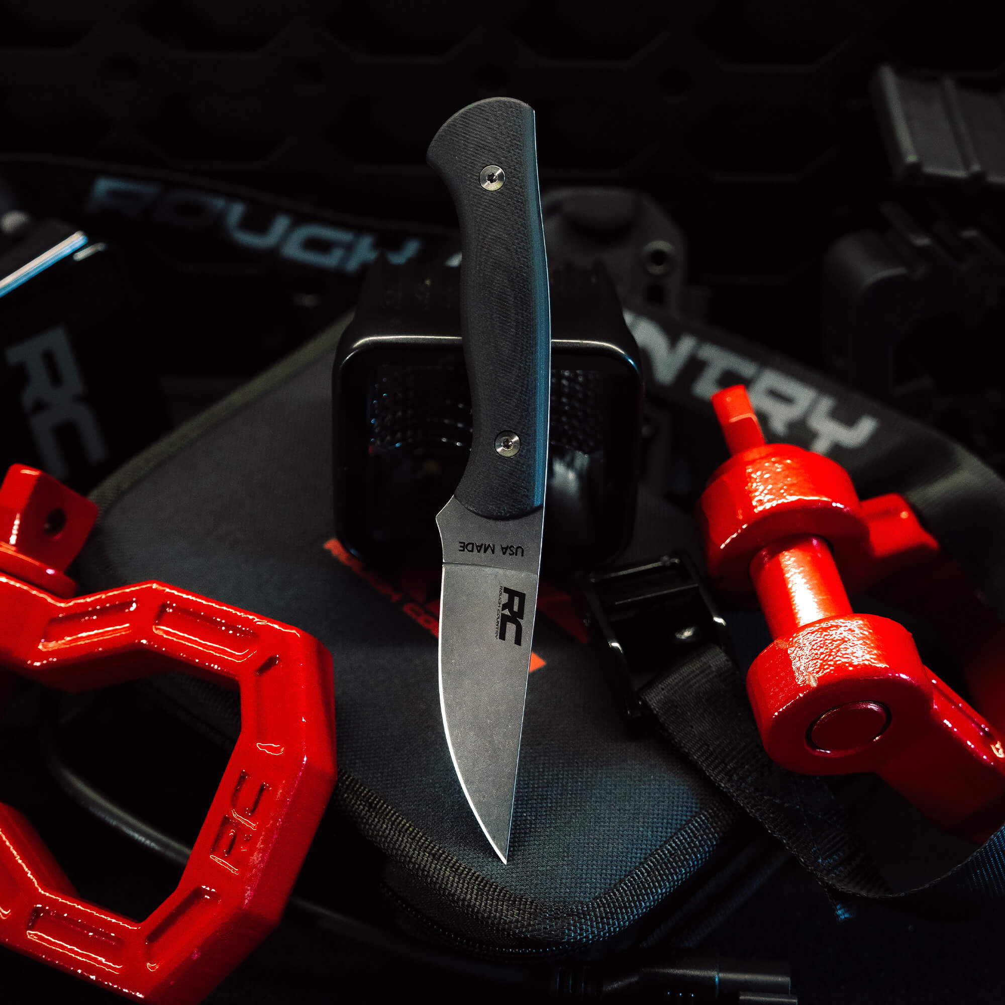 Rough Country Magnacut Blackfoot 2.0 knife displayed on a tactical background with red accessories, showcasing its sleek design.